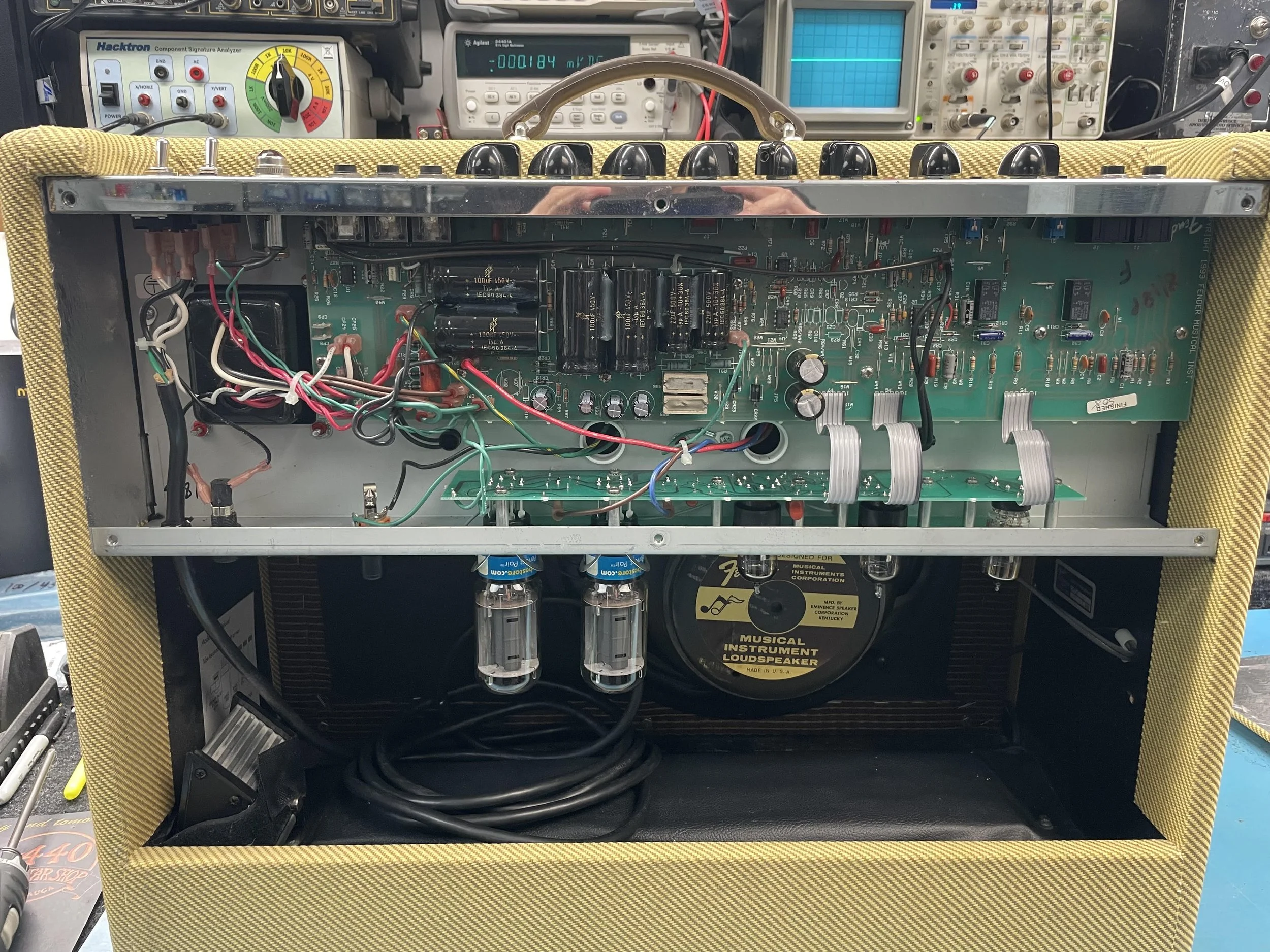 Close-up of an electronic musical instrument with exposed internal components, including circuit boards, wires, capacitors, and vacuum tubes. The instrument is partially covered with yellow fabric on the sides.