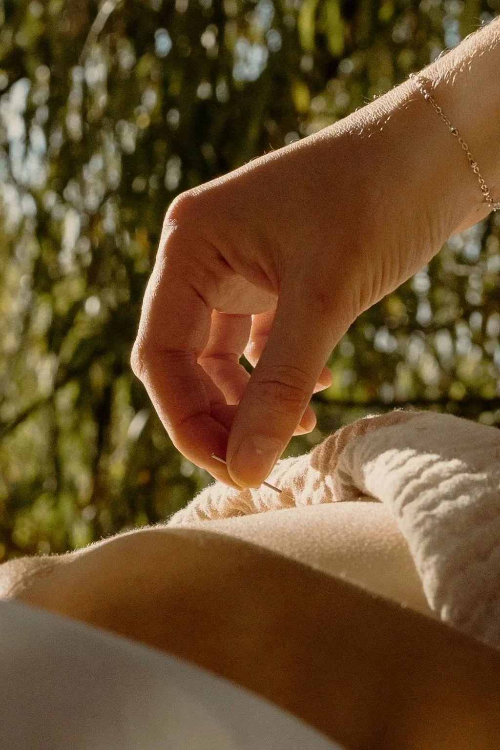 A close-up of a person receiving acupuncture treatment in a natural outdoor setting with blurred trees in the background.