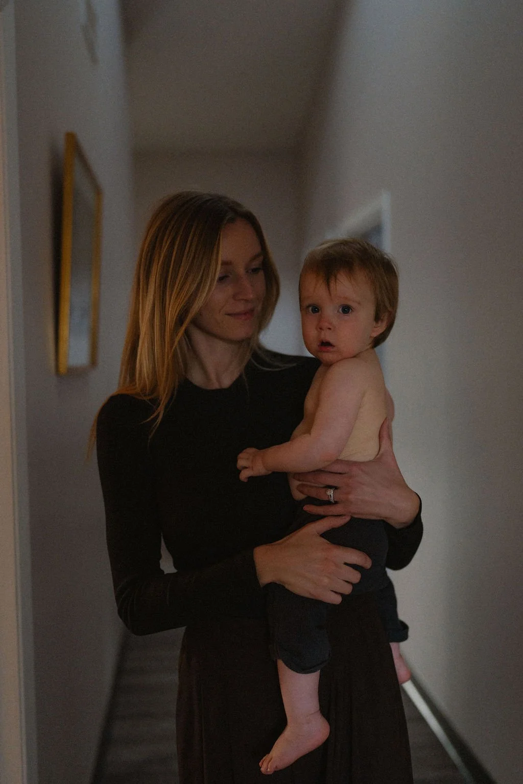 Dr. Hannah Zeleznikar, A woman with long, blonde hair, holding her young, shirtless son Teddy with brown hair in the hallway of Yinergy Acupuncture.