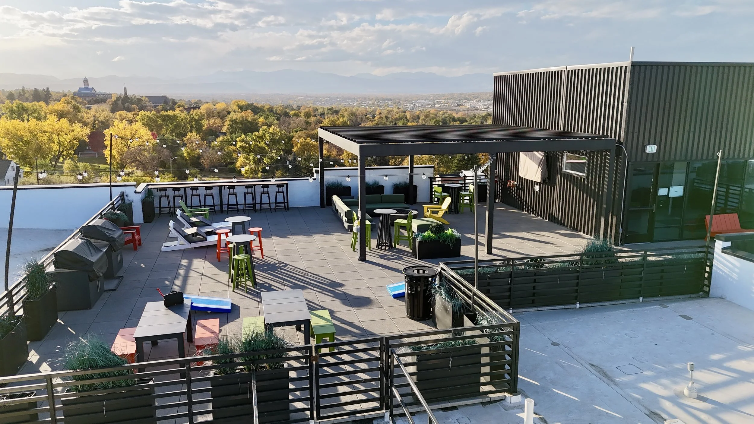 Rooftop patio with outdoor seating, bar area, string lights, and scenic view of trees and mountains in the distance.
