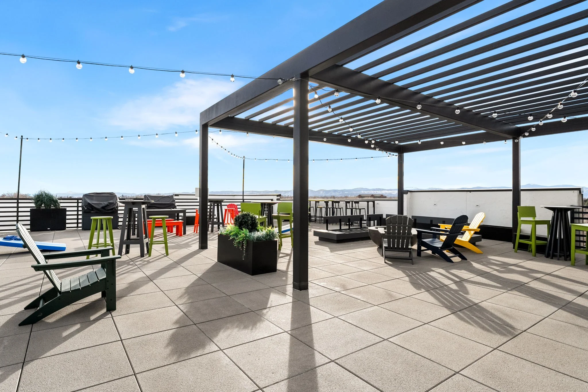 Rooftop patio with outdoor furniture, string lights, potted plants, and mountain view in the background on a clear day.
