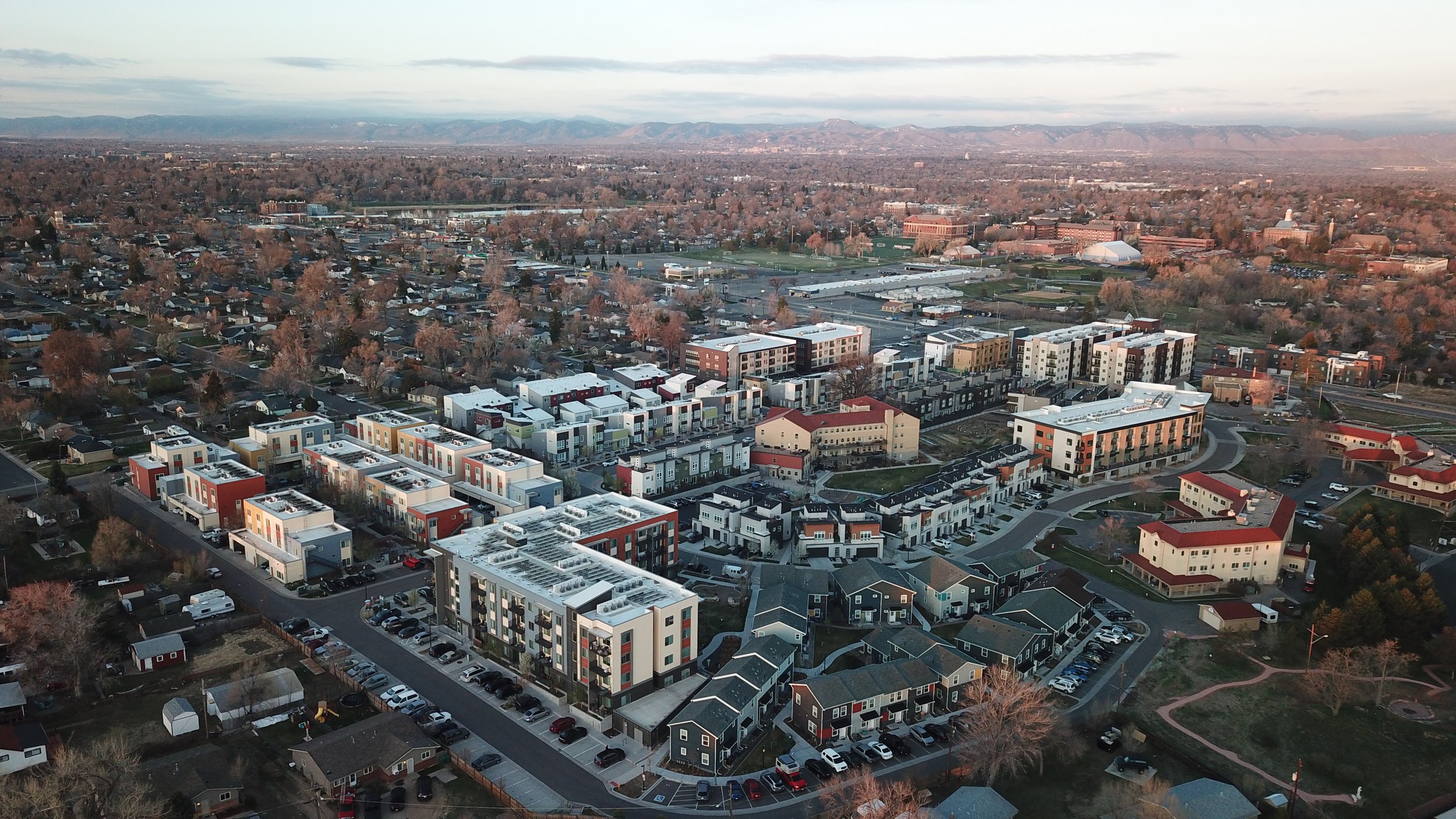 Aerial view of a suburban area with modern apartment buildings, residential houses, roads, and trees, with mountain range in the background.
