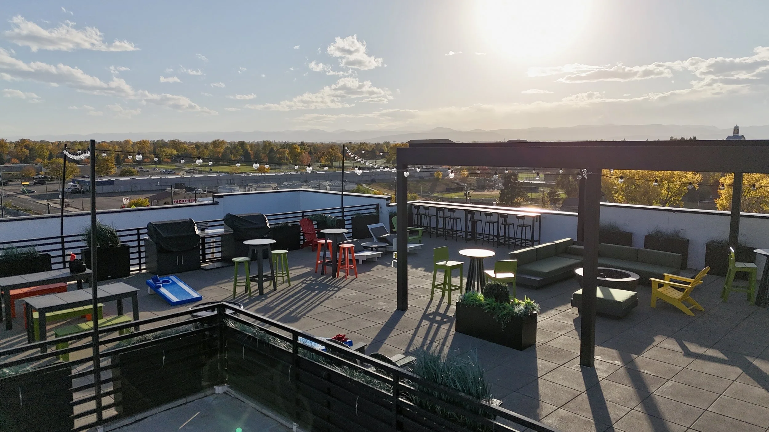 Rooftop patio with seating and tables, string lights, and city view in sunset.