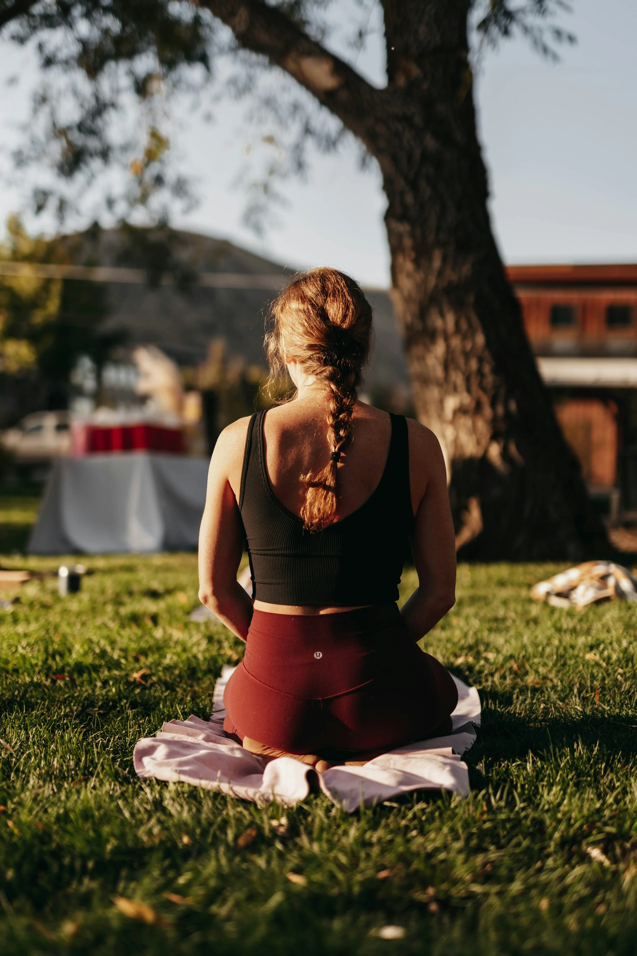 A woman with a braid is seated alone on a blanket in the park.