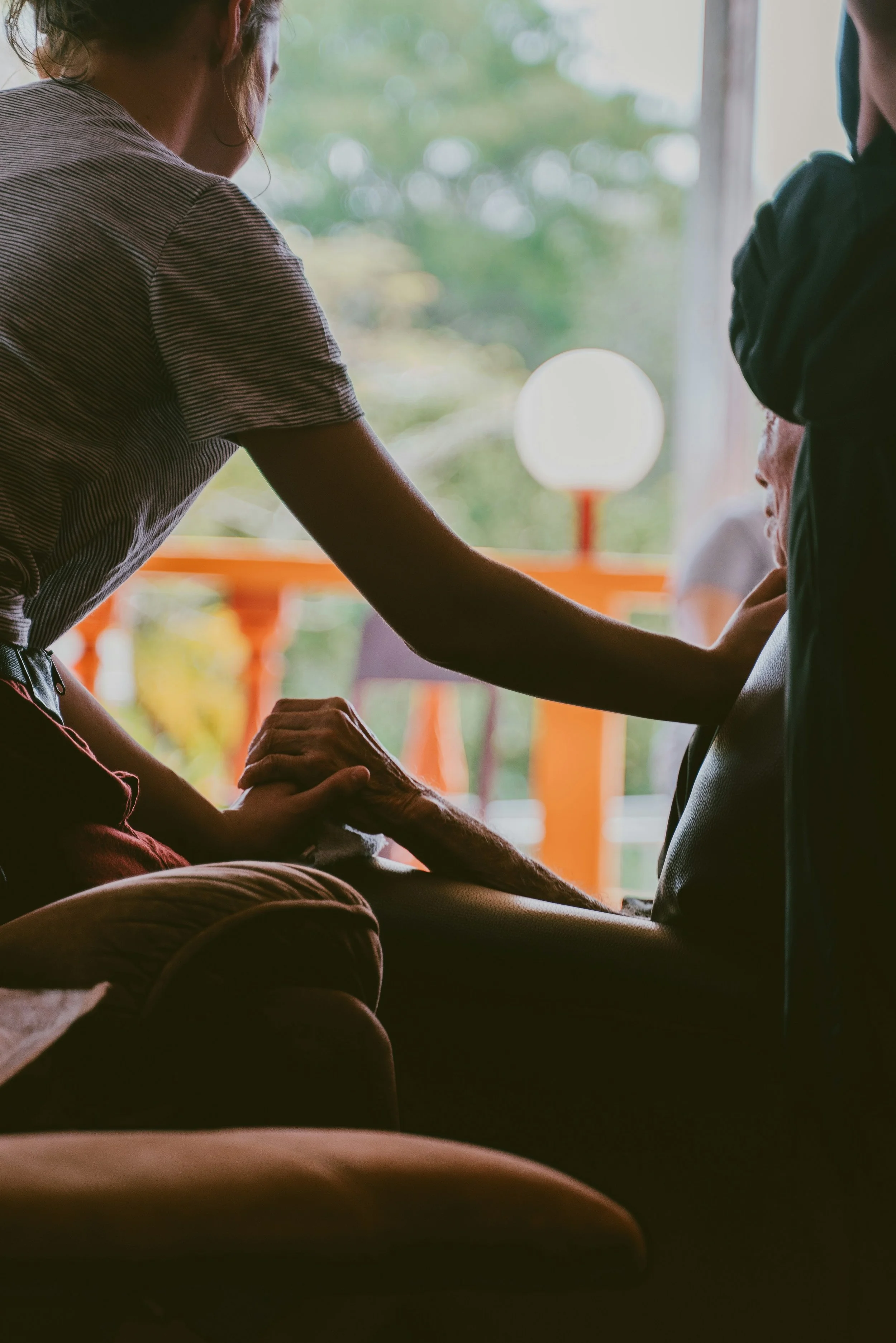 Two women hold hands as the younger woman places her hand against the older woman's heartin a steadying, soft touch.