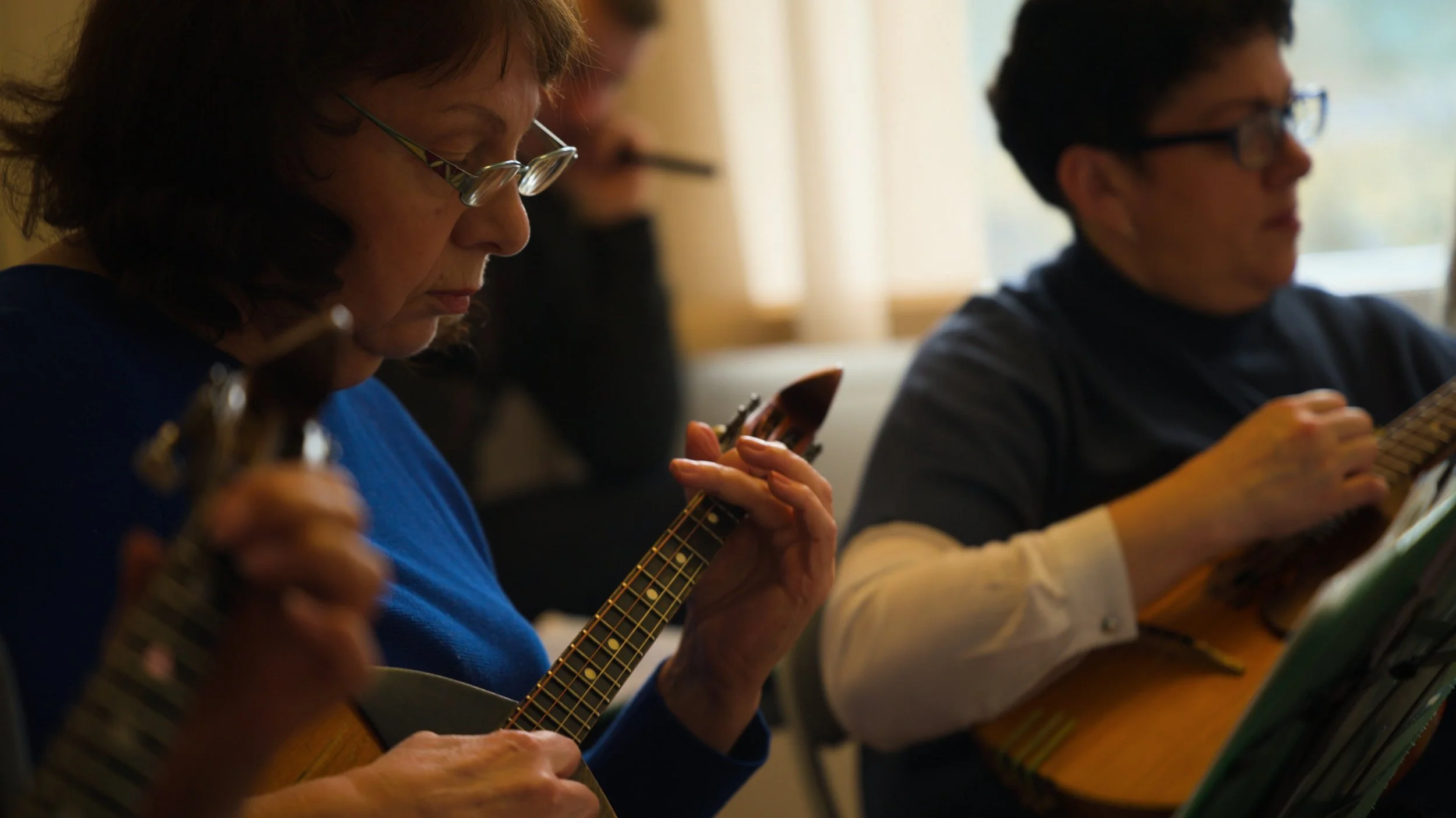 Two women playing traditional Ukrainian stringed instruments during a music session inside a room with natural light.
