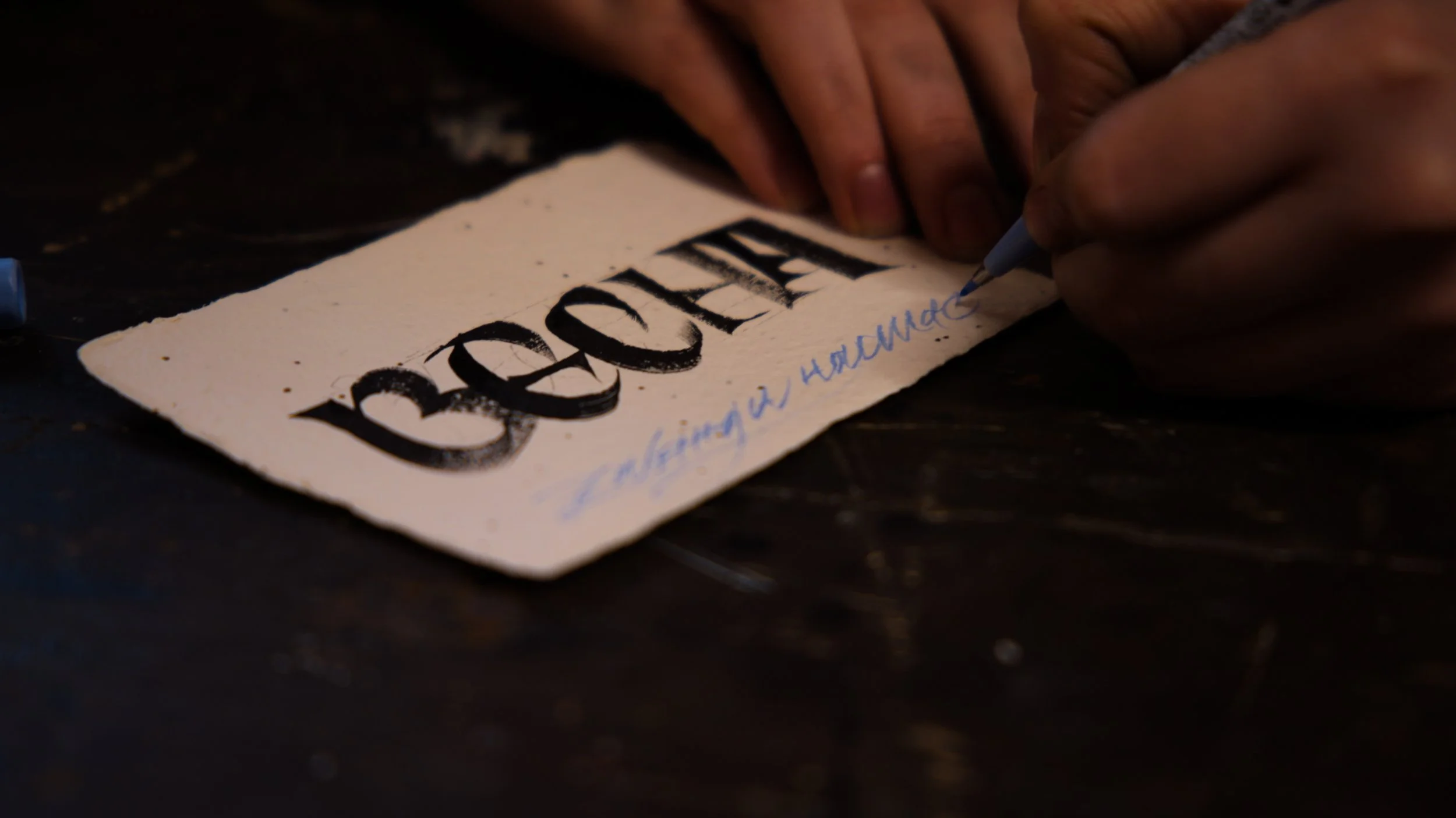 Close-up of hands writing on a piece of paper with a blue pen. The paper has a large, bold word 'ВЕСНА' written in black and some smaller blue text underneath.