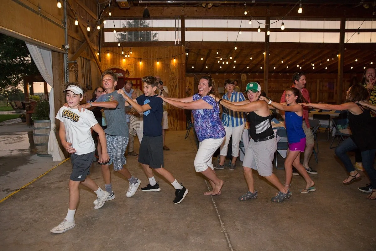 People playing a game of tug-of-war indoors with string, smiling and laughing, illuminated by string lights.