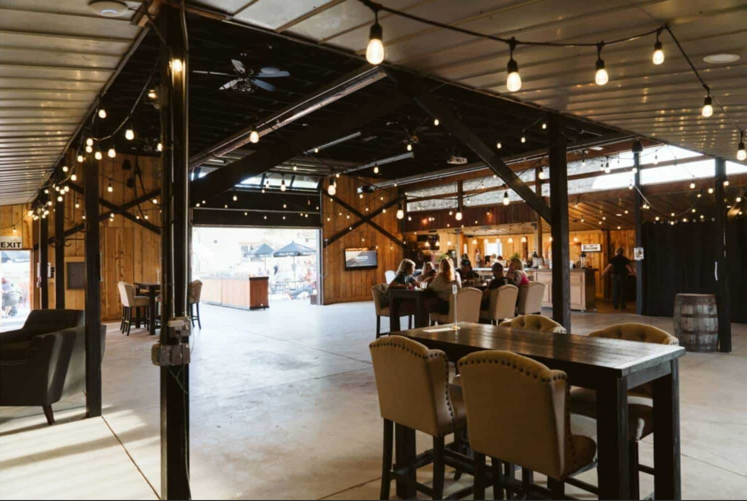 Large rustic indoor event venue with wooden walls and string lights on the ceiling