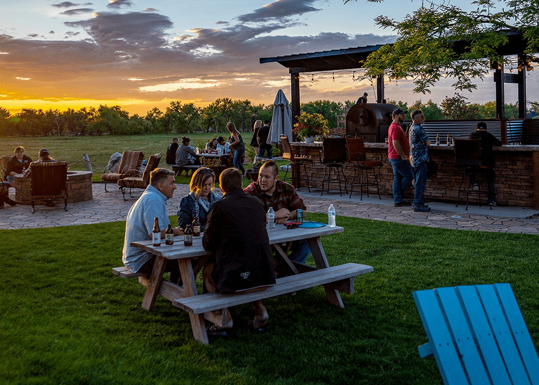 People enjoying outdoor gathering with barbecue and sunset sky.