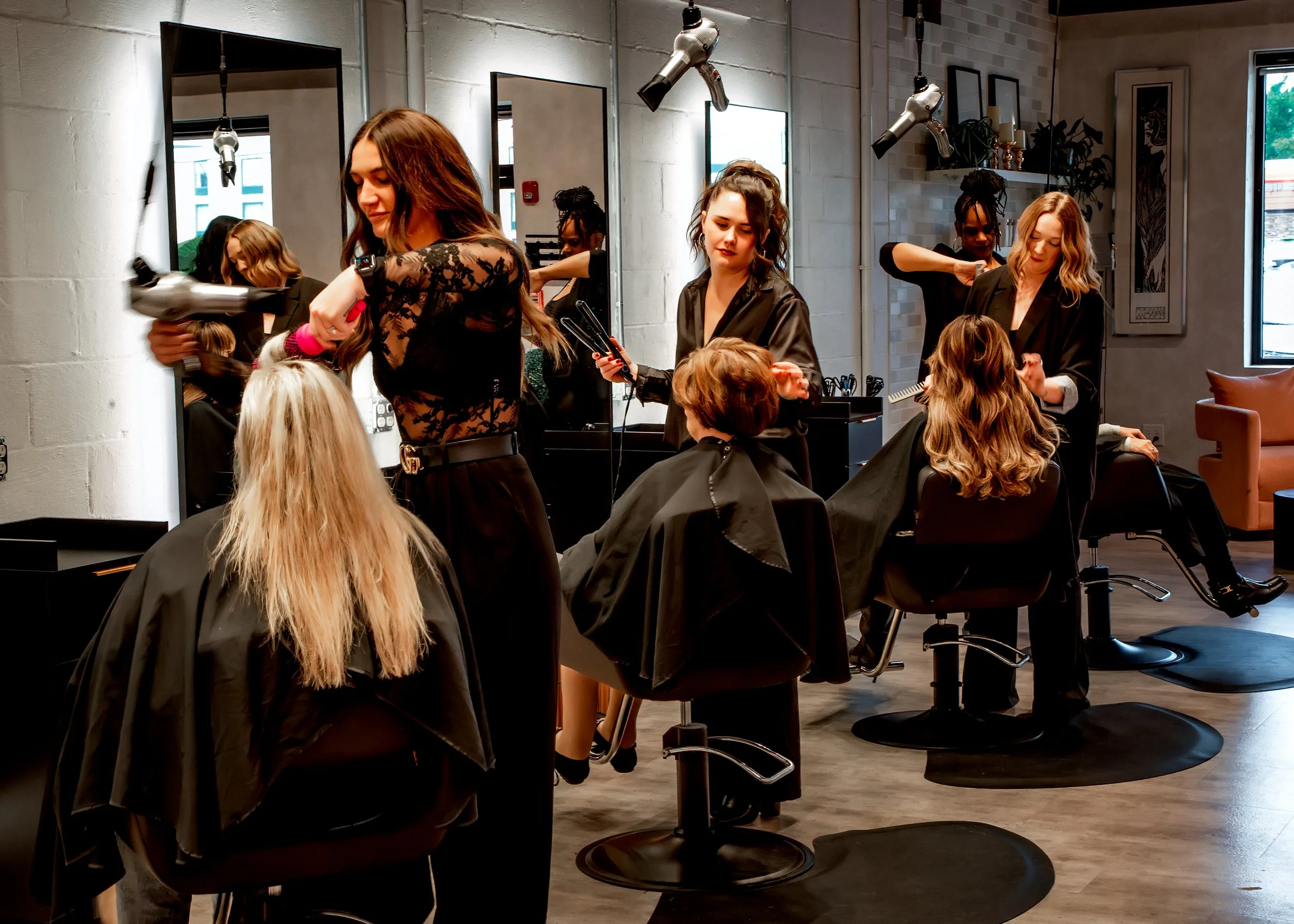 Women at hair salon getting styled and haircuts, with hairstylists working on clients.