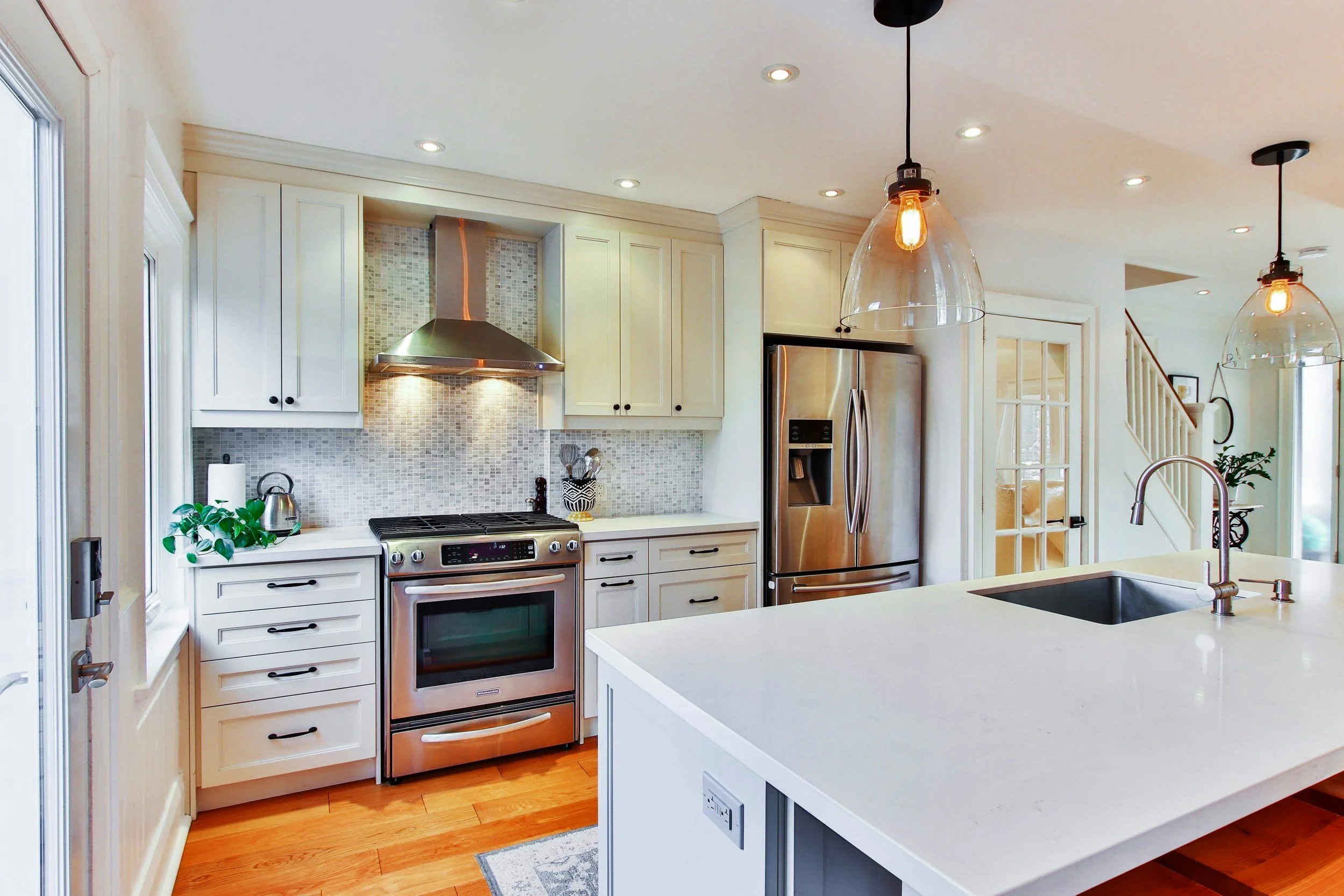 Modern kitchen with white cabinets, stainless steel appliances, pendant lights, and an island with a sink.