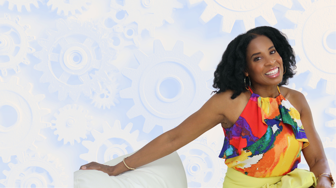 Dara Fairman smiling and sitting on a white chair, wearing a colorful sleeveless top and yellow skirt, with a background of white gears and cogs.