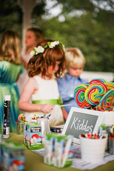 Children at a birthday party with colorful lollipops, candy, and a chalkboard sign that says 'Kiddos'.