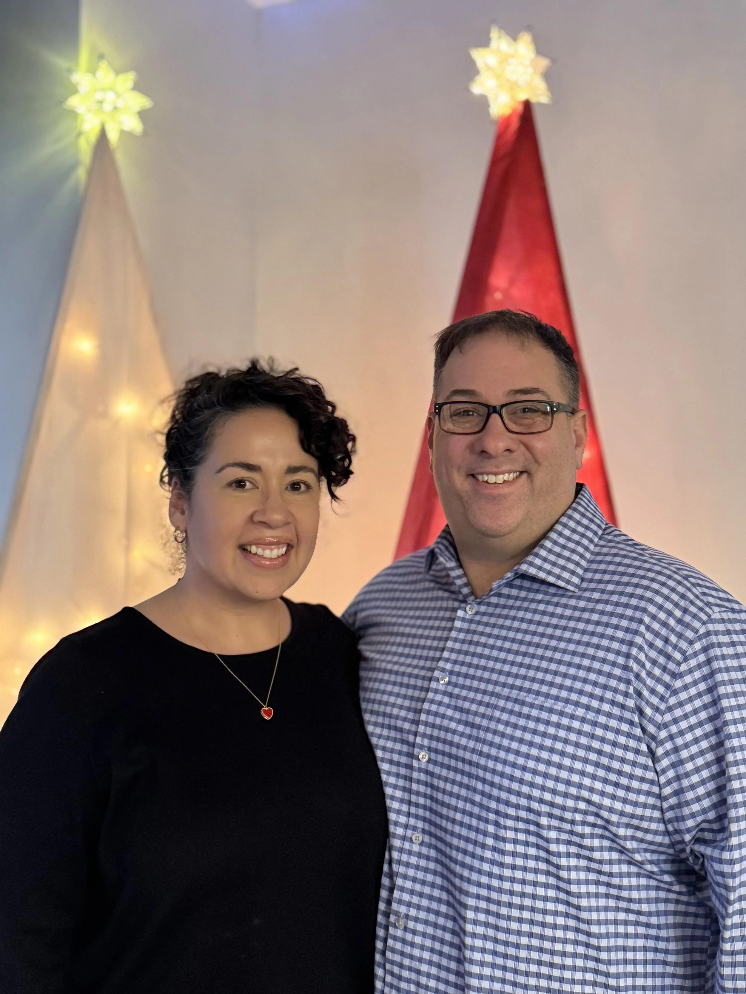 A smiling couple standing in front of decorated Christmas trees with star toppers