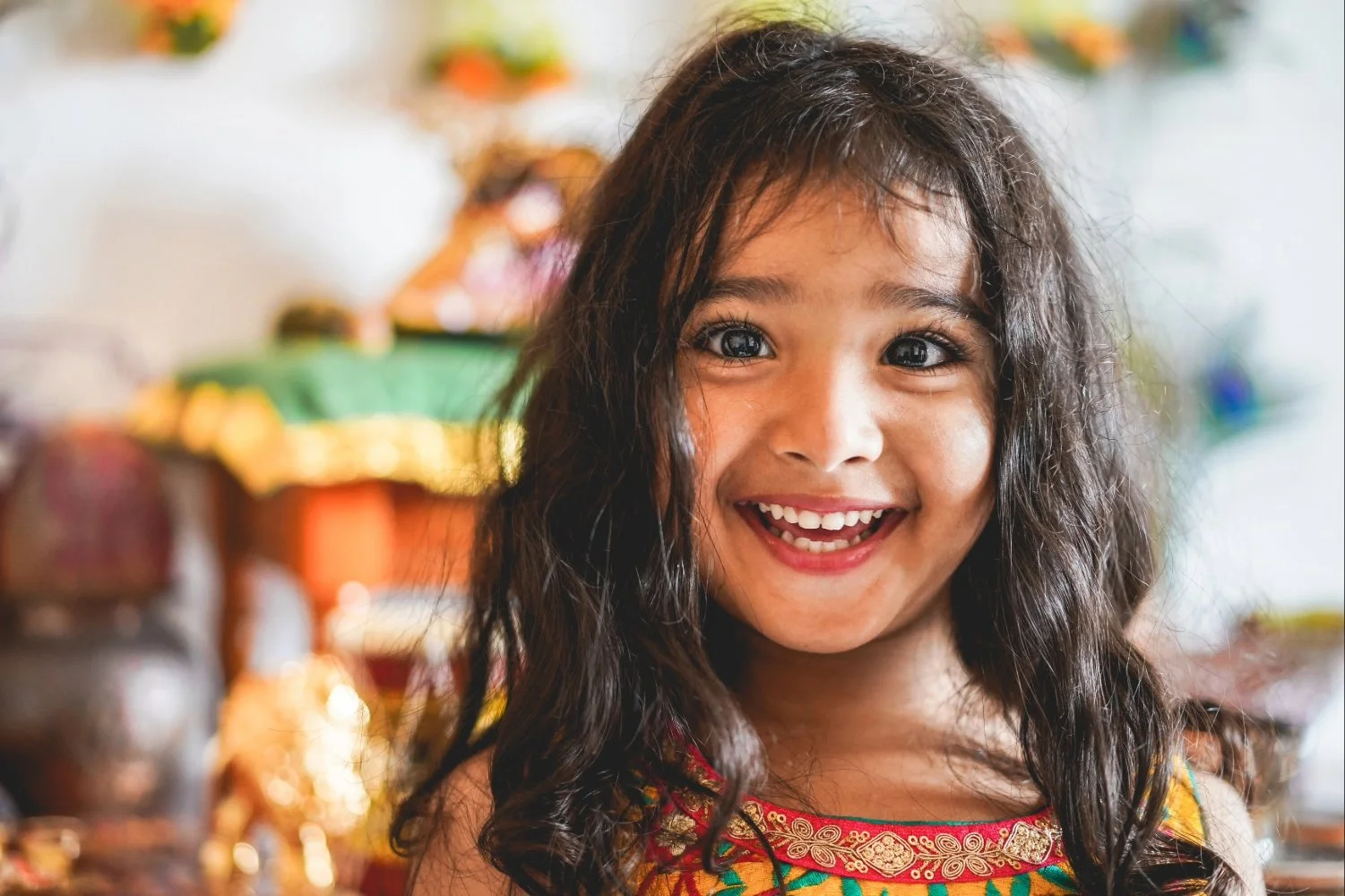 A young girl with dark hair and bright eyes, smiling and wearing a colorful traditional dress, who is receiving culturally responsive speech therapy for kids in Laurinburg, NC.