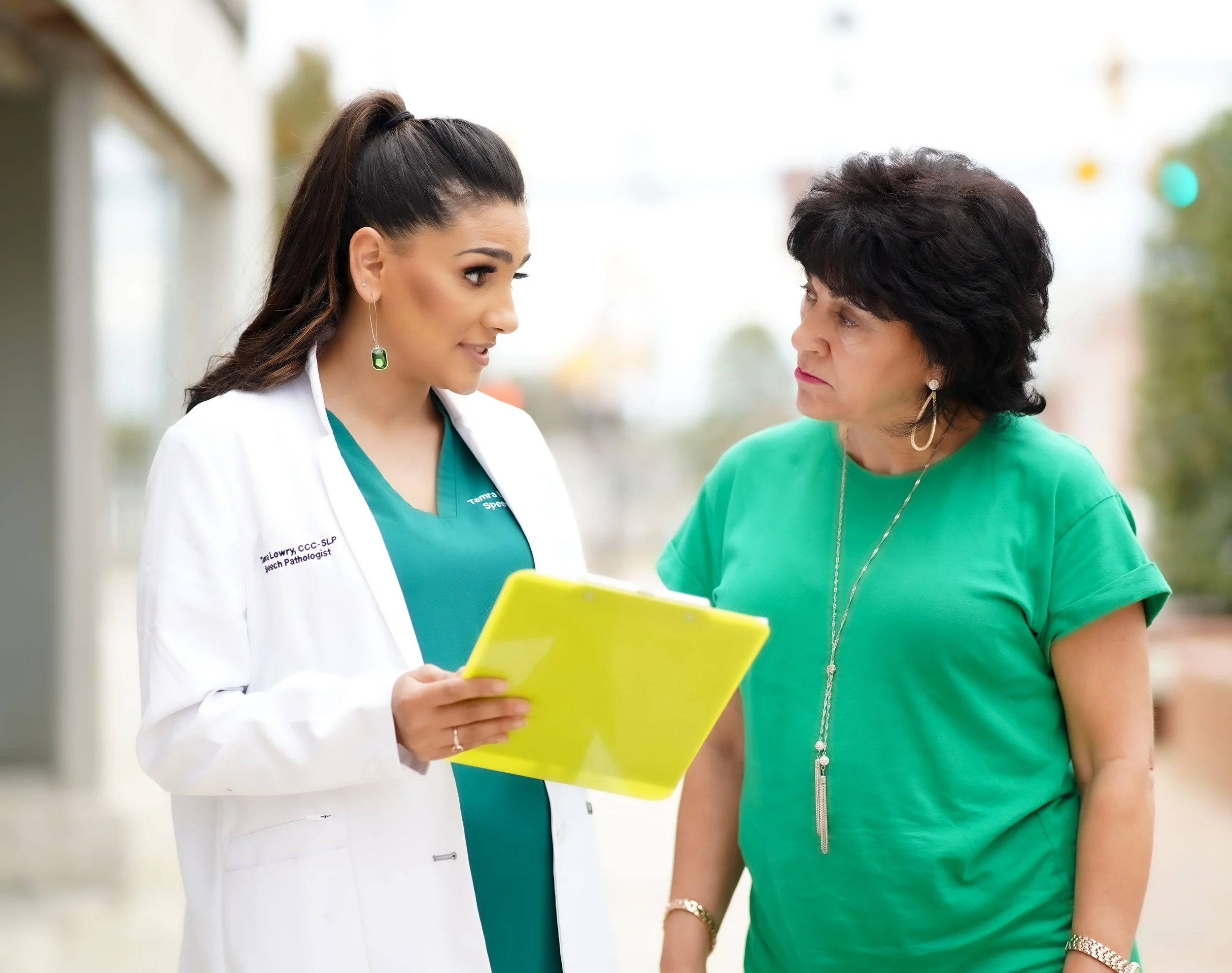 A speech therapist for adults and a woman are standing outdoors having a conversation, with the speech therapist showing information on a yellow tablet and providing education about caring for a loved one after a stroke in Laurinburg, NC.