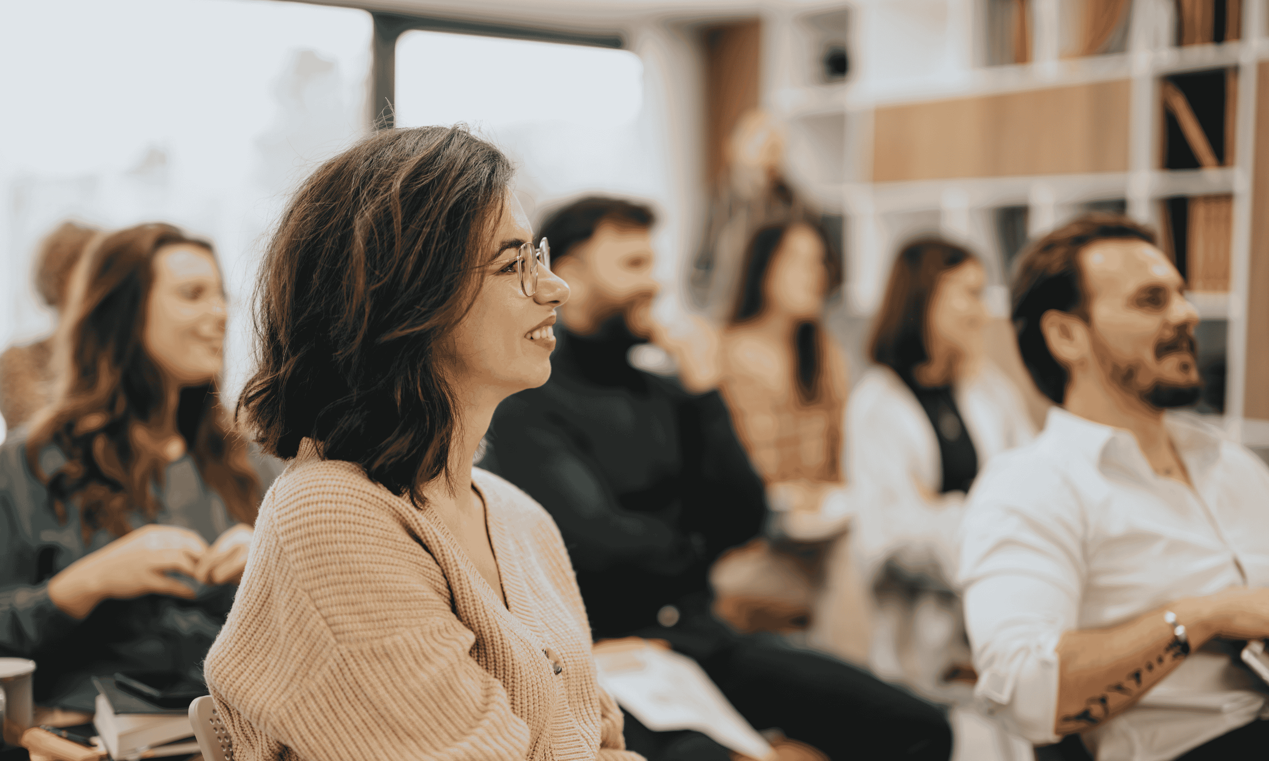 A group of people attending a workshop in a bright room, with a woman in the foreground smiling and listening attentively to a speech therapist providing DEI training for healthcare professionals in North Carolina.