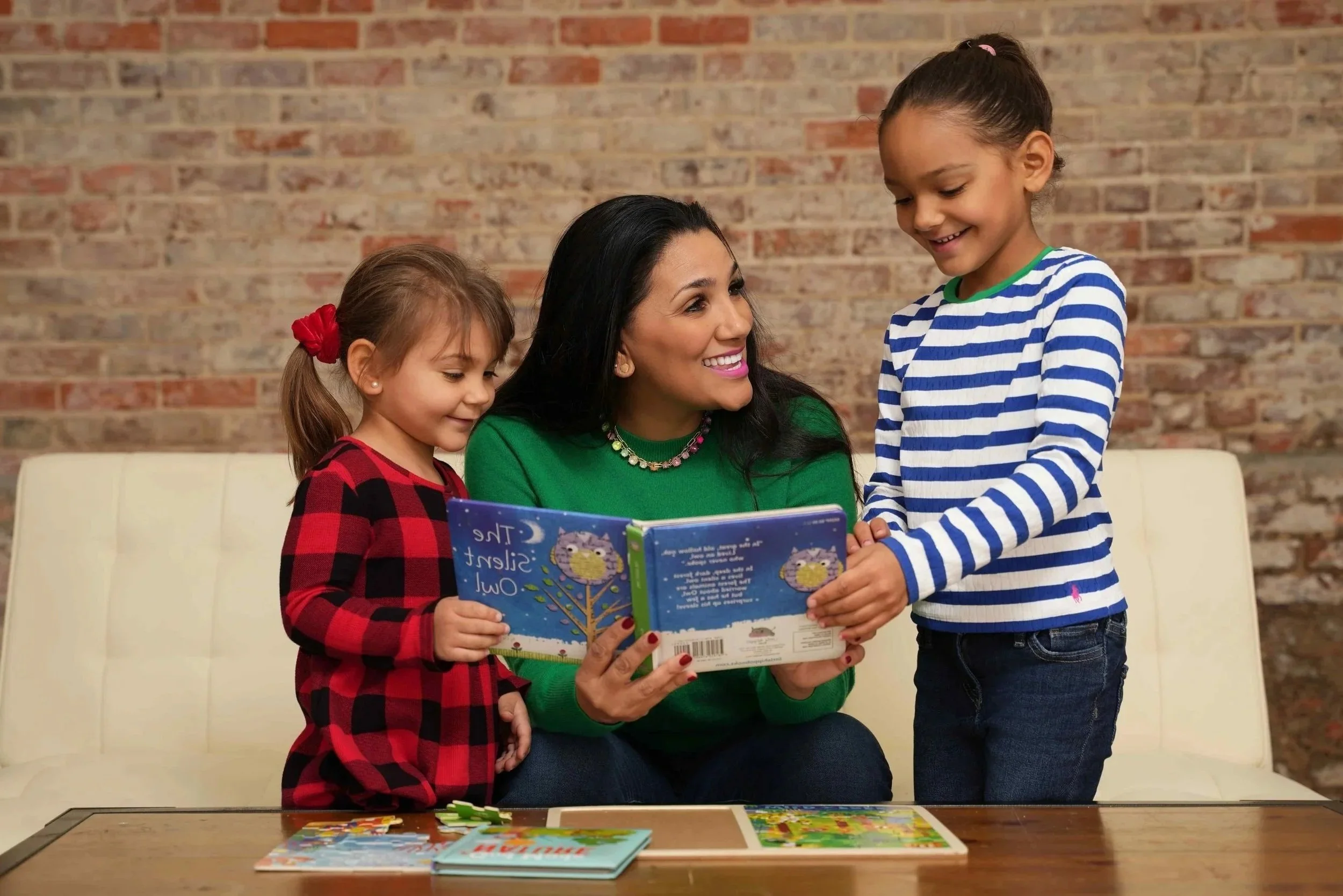 A speech therapist is sitting on a white bench reading a children's book to two young girls during speech therapy for children in Laurinburg, NC.