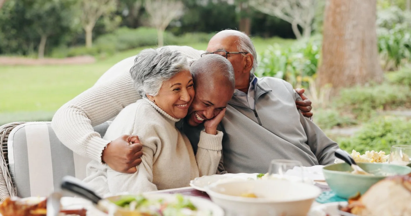 An elderly woman and two adult family members sharing a joyful hug at an outdoor meal. The woman is able to enjoy mealtimes again after swallowing therapy for adults in Laurinburg, NC.