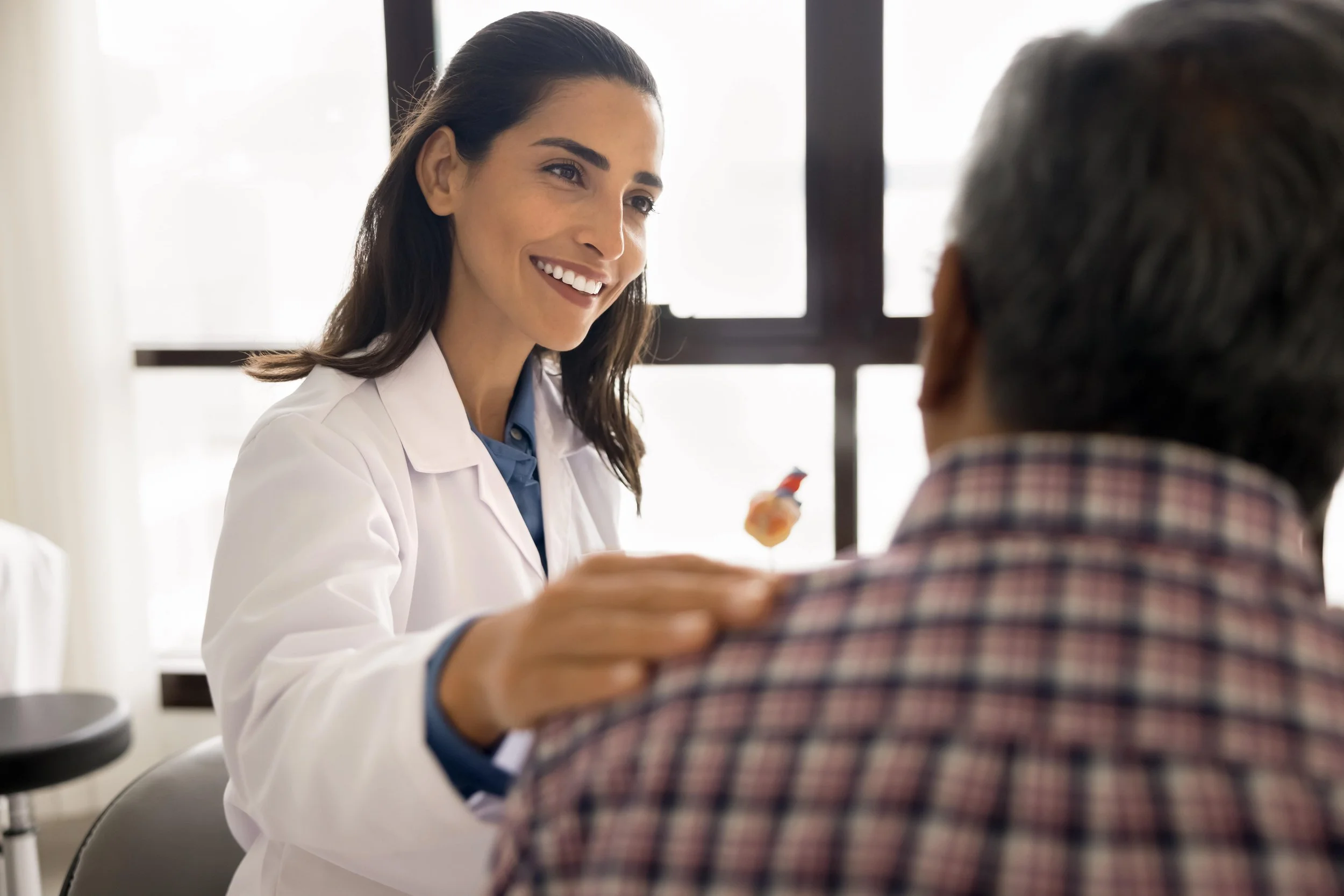 A female speech therapist for adults smiling and talking to an older male patient in a medical office, discussing swallowing and cognitive therapy after stroke in Laurinburg, NC.