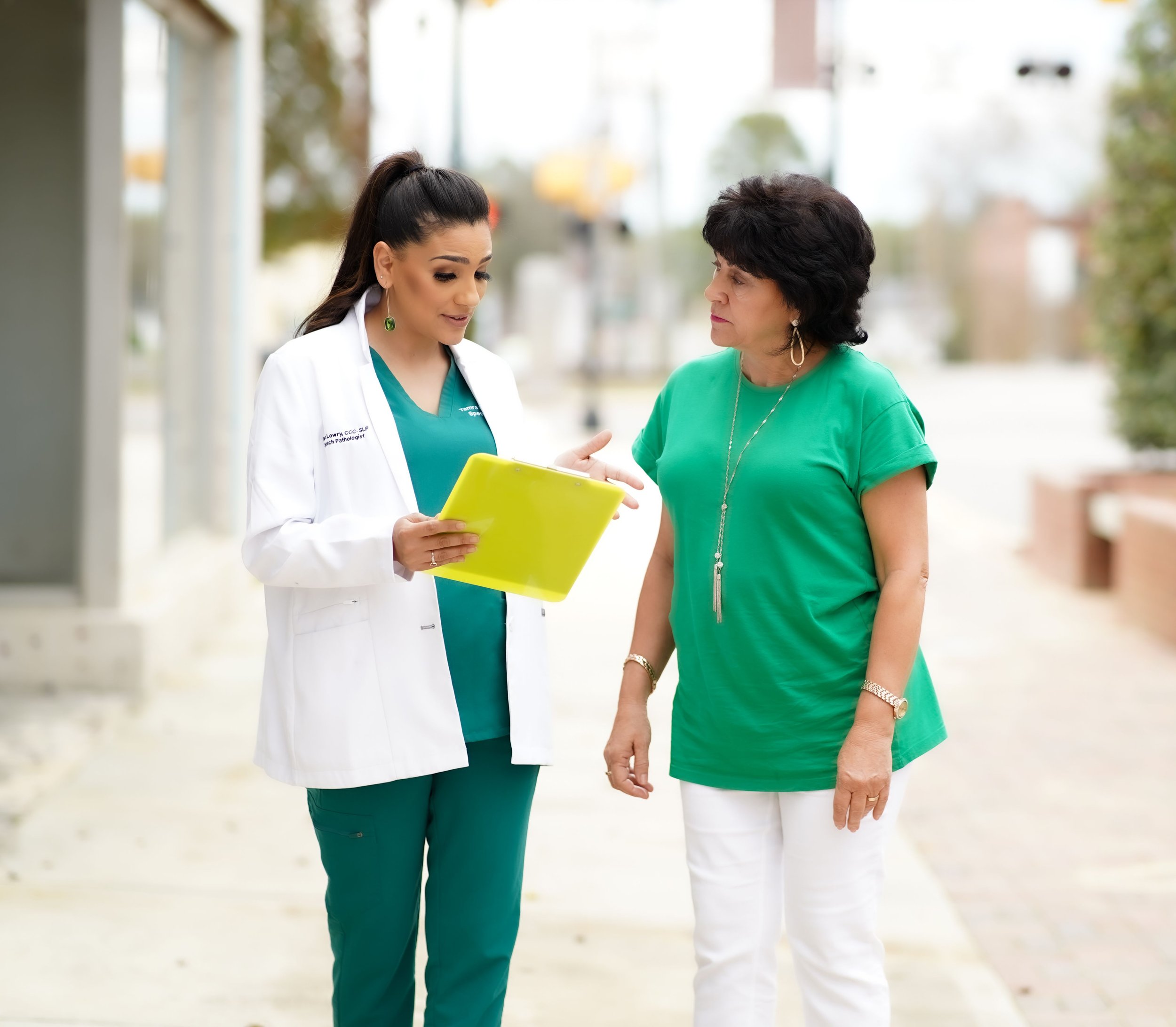 A speech therapist for adults and a woman are standing outdoors having a conversation, with the speech therapist showing information on a yellow tablet and providing education about caring for a loved one after a stroke in Laurinburg, NC.