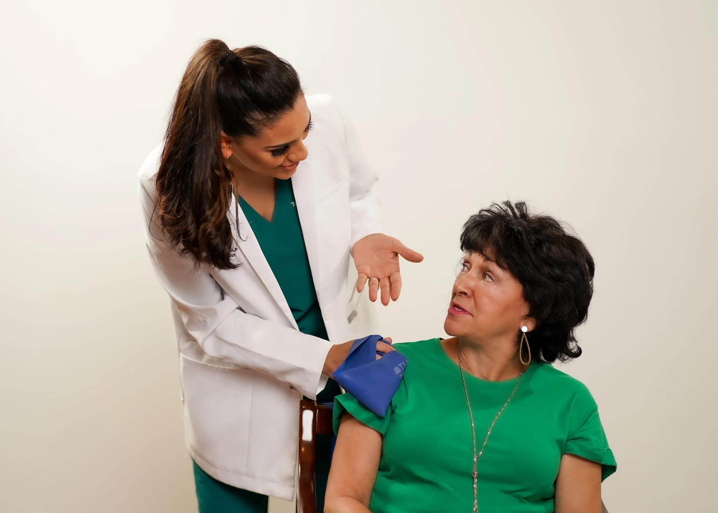 A speech and swallowing therapist for adults talking to a woman in a green shirt in a clinical setting about swallowing evaluation using FEES.
