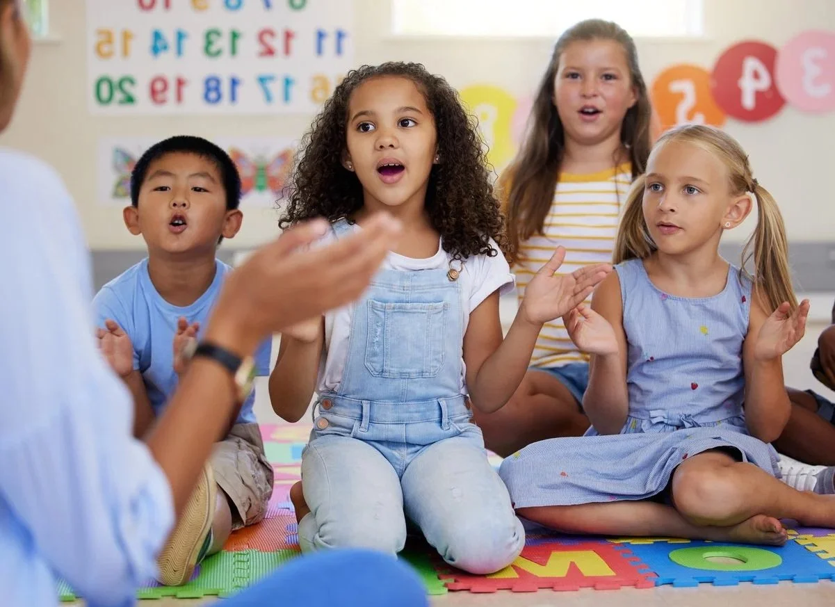 Children sitting on a colorful foam mat in a classroom, engaging in a singing activity with a contract speech therapist in North Carolina.