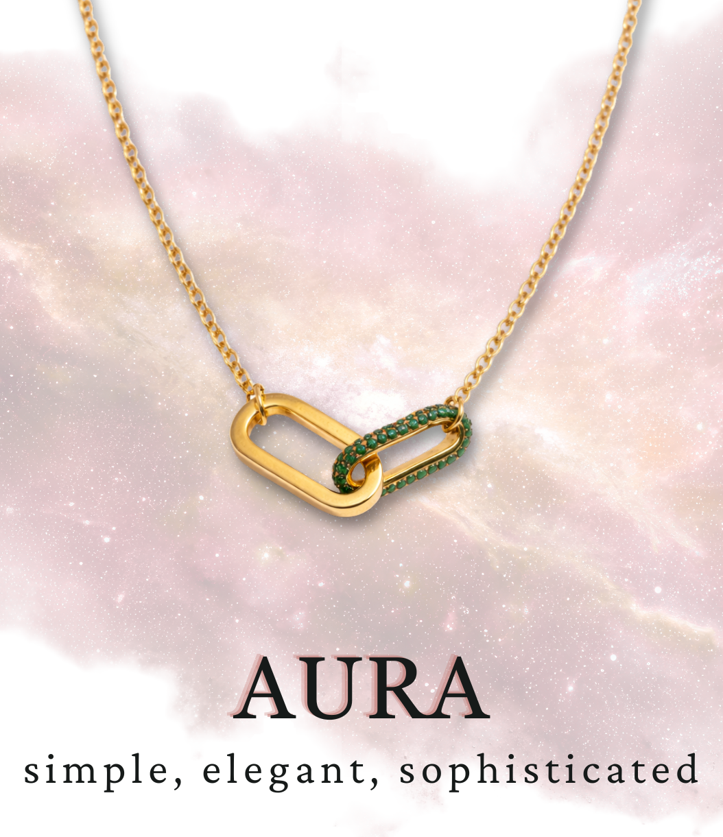 Gold necklace with intertwined oval links, one set adorned with green stones, displayed against a soft pink and white background with sparkles.