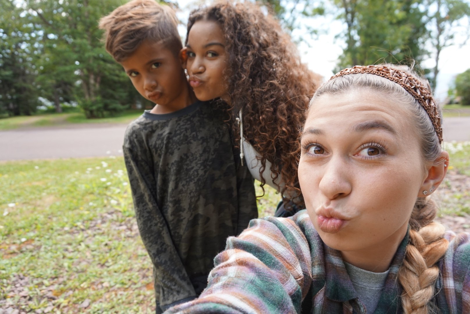 Three children taking a selfie outdoors in a park with trees in the background.