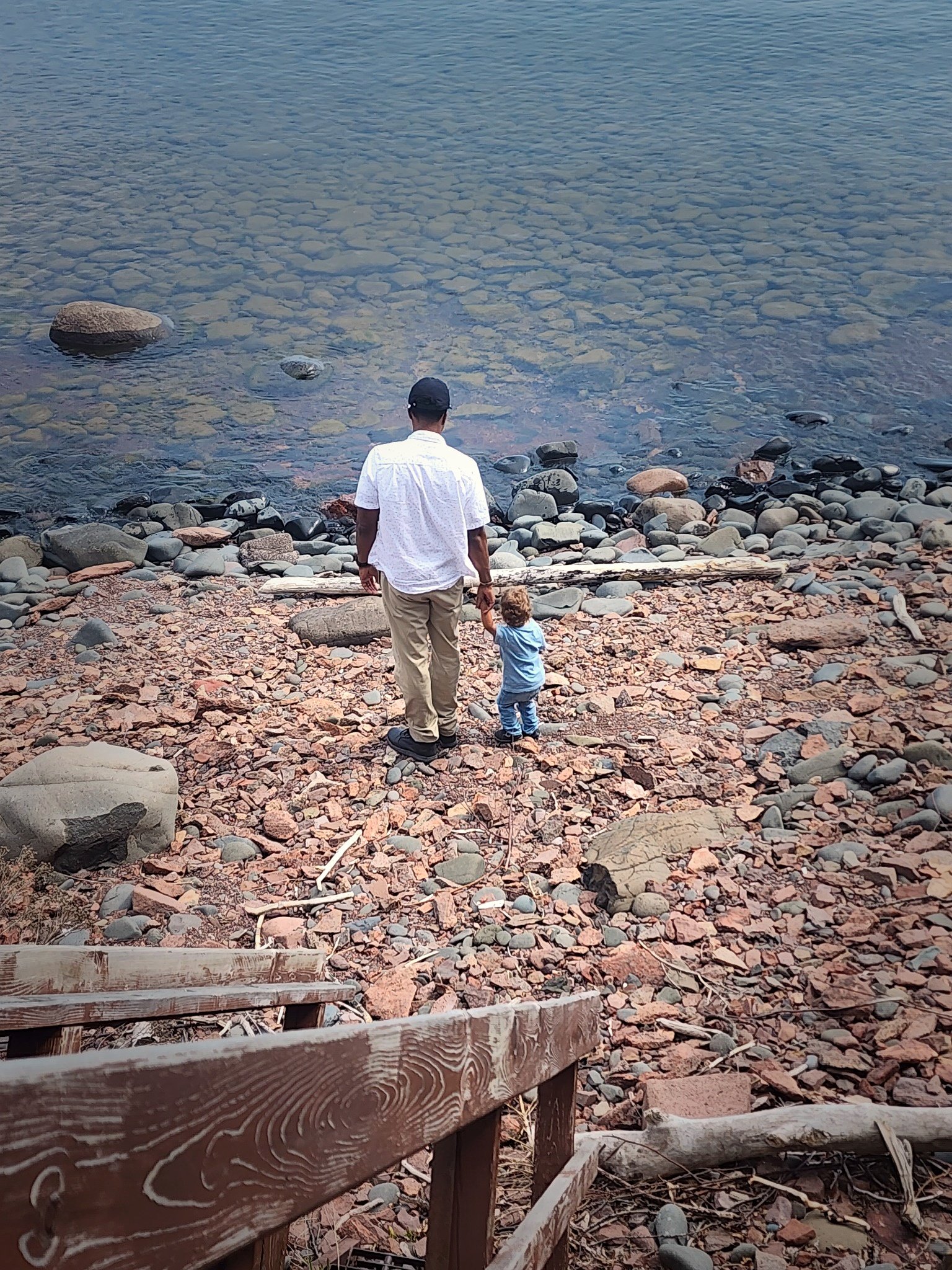Man and young child walking on rocky shoreline by a lake