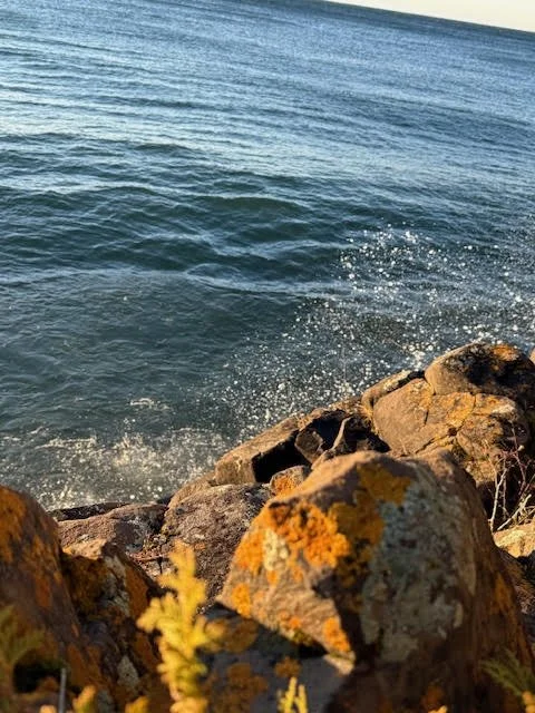 View of ocean waves crashing against rocks along the shoreline at sunset.