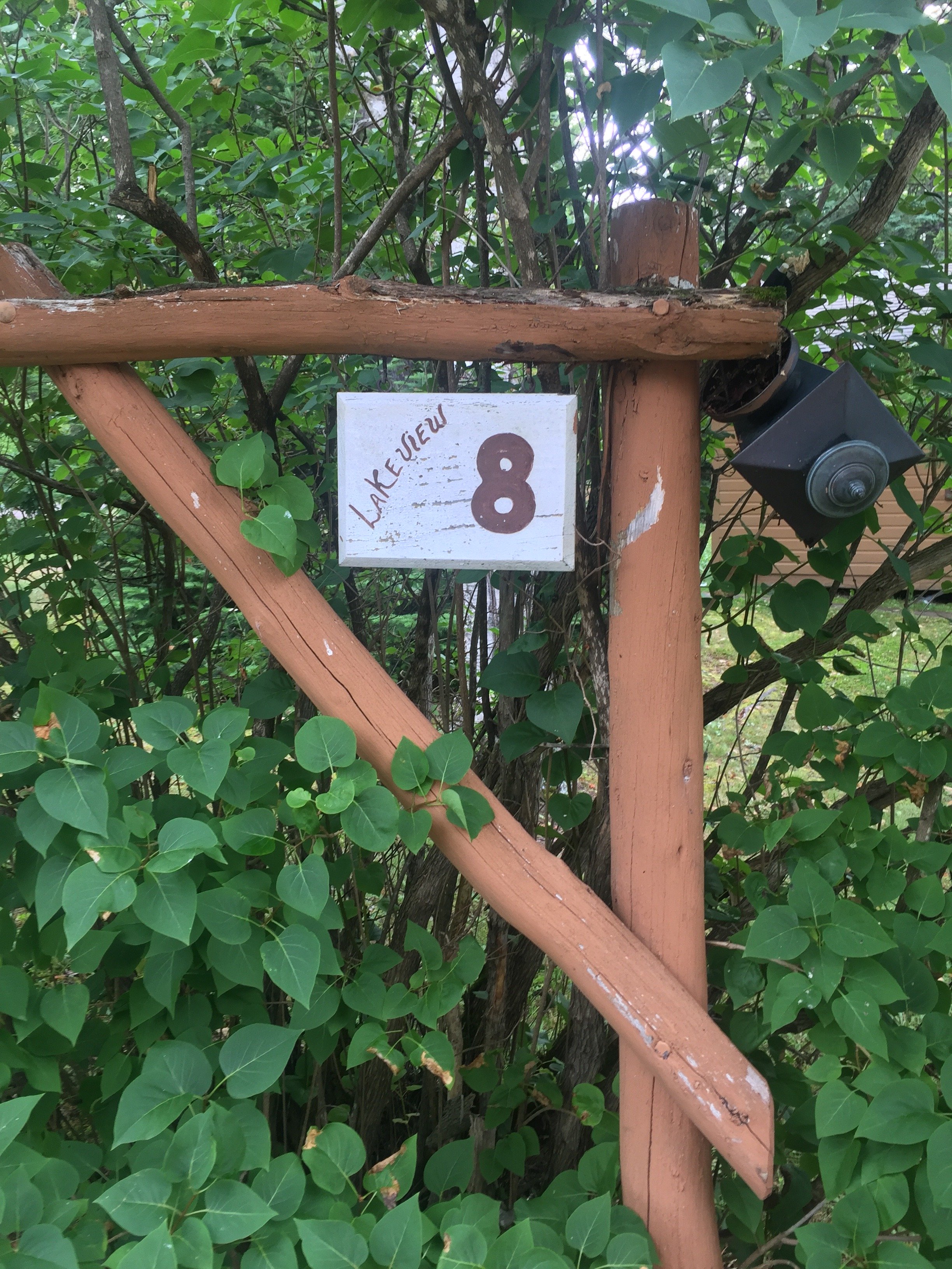 Wooden sign attached to a fence with a latch, surrounded by green leaves, displaying the number 8 and the words 'Lakesview' in red.