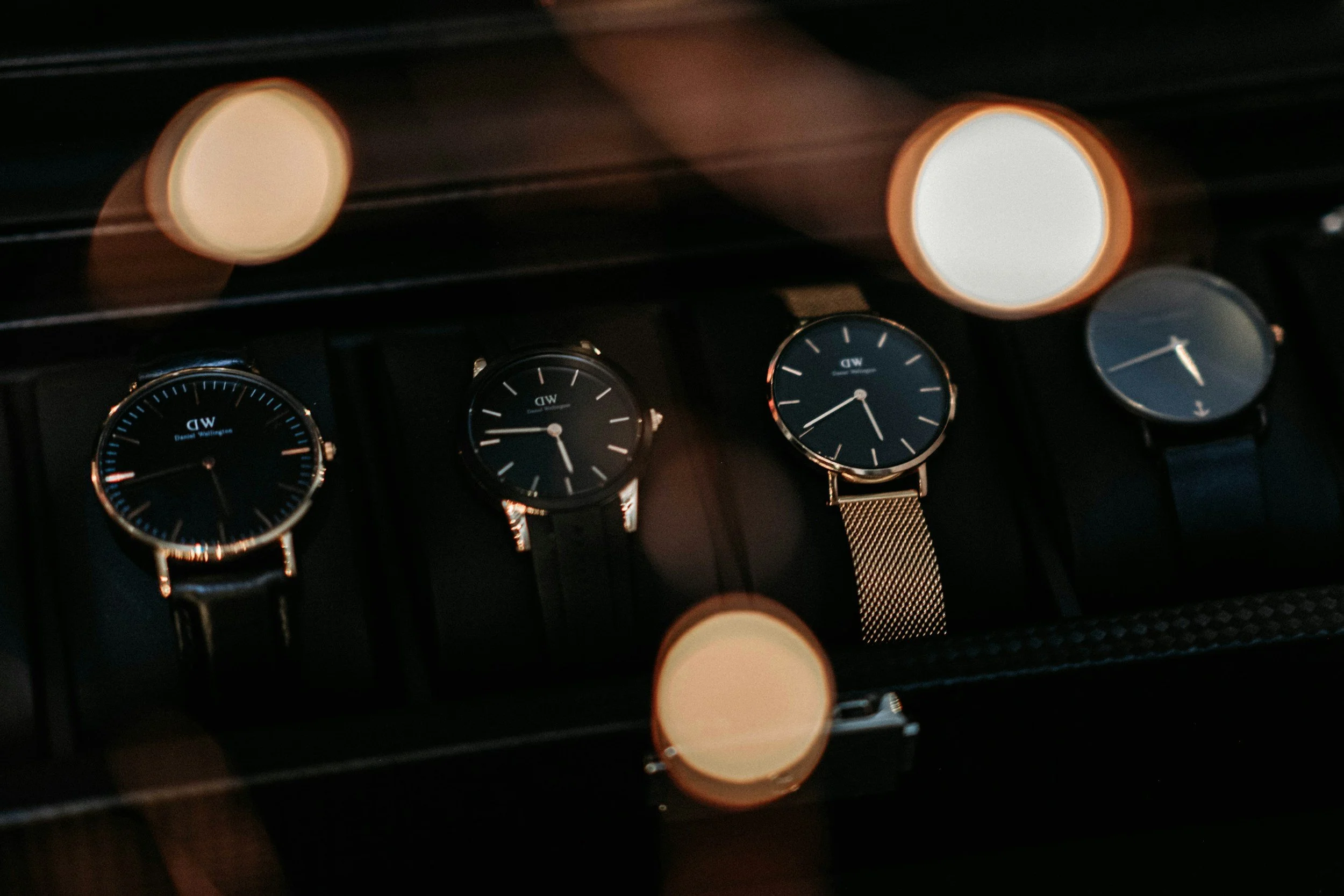 Billede af flere armbåndsure i forskellige stilarter og urværker, der er placeret i en række, med nogle store bløde lysende cirkler i baggrunden.