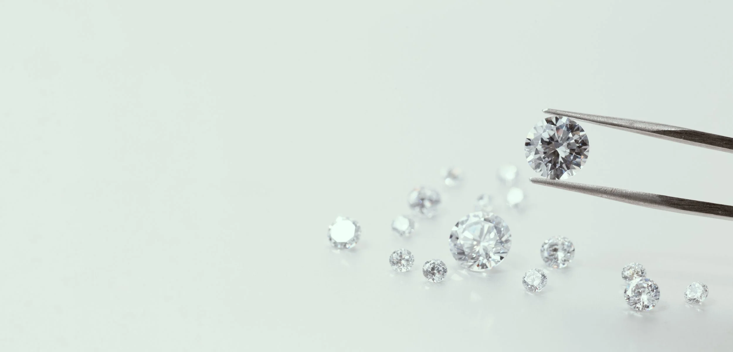 Diamantbryllup med en stor rund brillant diamant, holdt af twe pincet, omgivet af mindre diamanter på en lys baggrund.