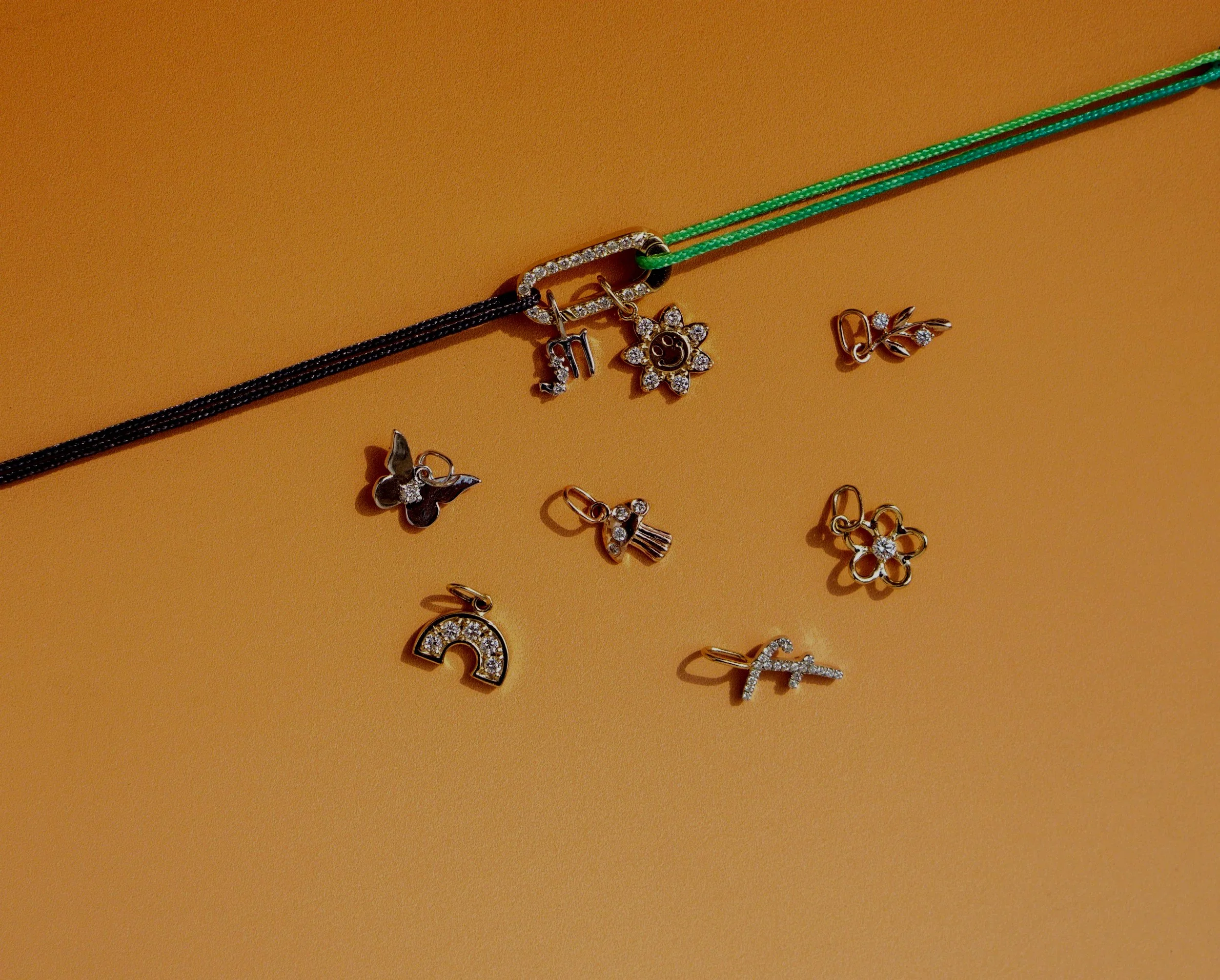 Billede af forskellige smykker, herunder halskæder og øreringe med charms, lagt ud på en beige baggrund.