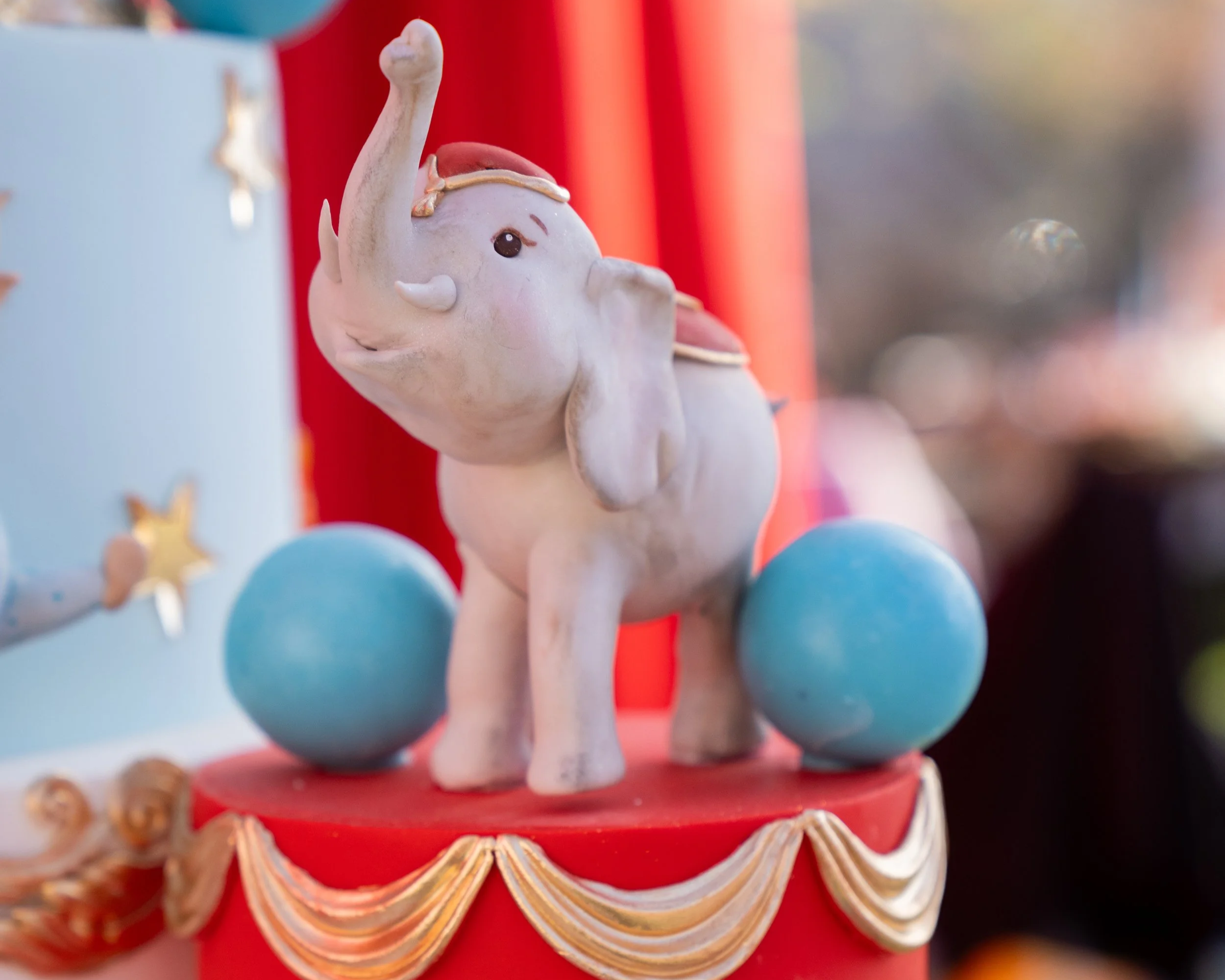 Decorative elephant figurine on a red surface with gold trim, positioned between two large blue balls, with a light blue and red background.