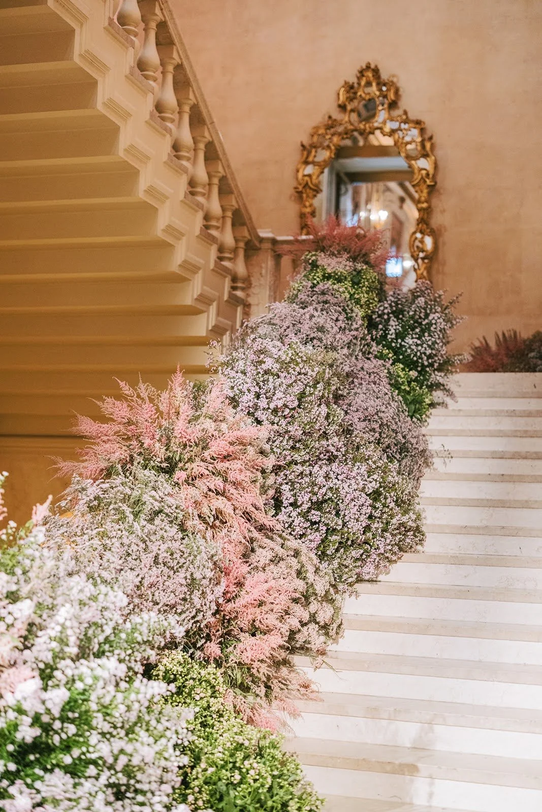 Decorative floral arrangement with pink and white flowers along staircase in elegant interior with gold-framed mirror