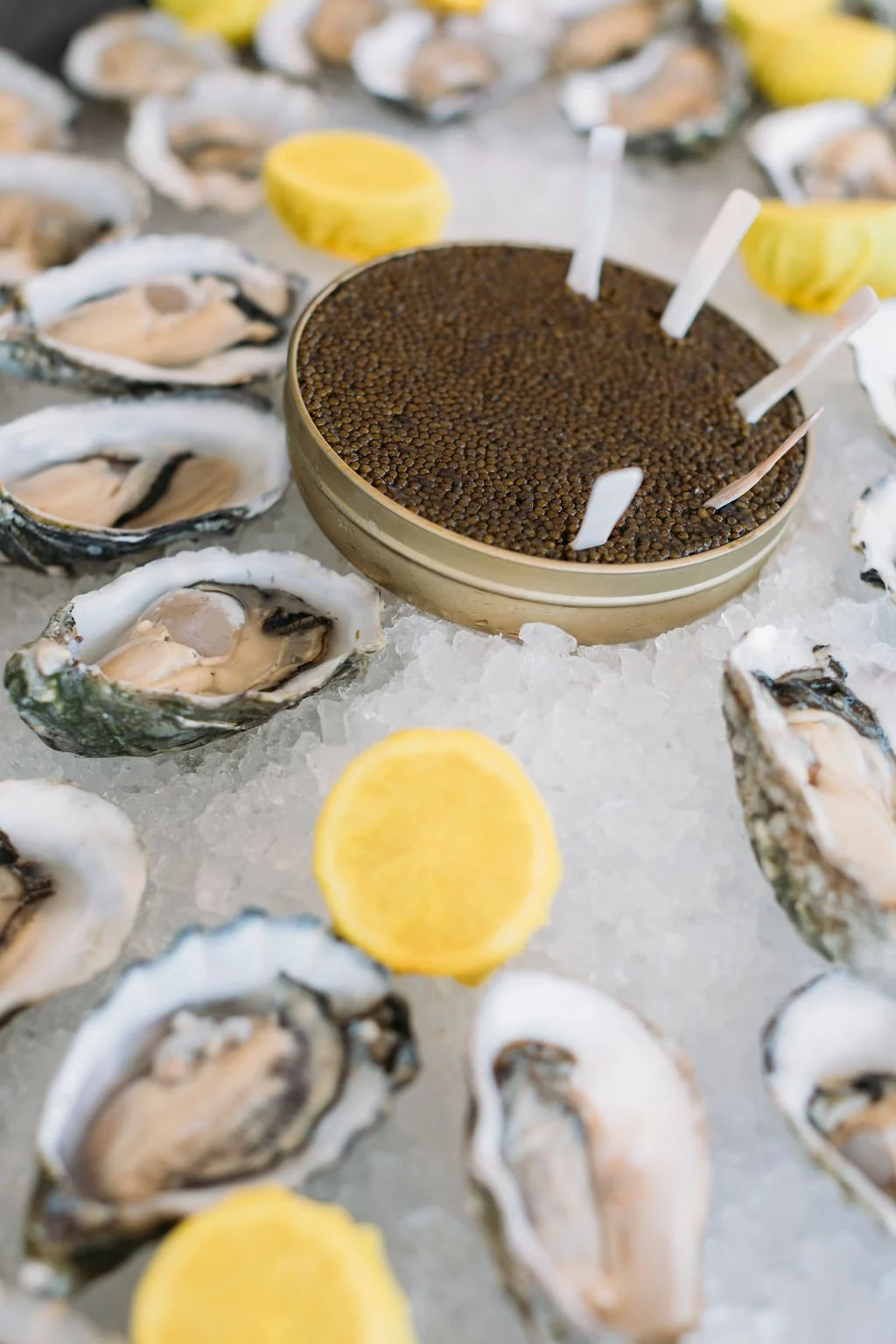 A bowl of fresh oysters on ice with lemon wedges and a tray of brown caviar.