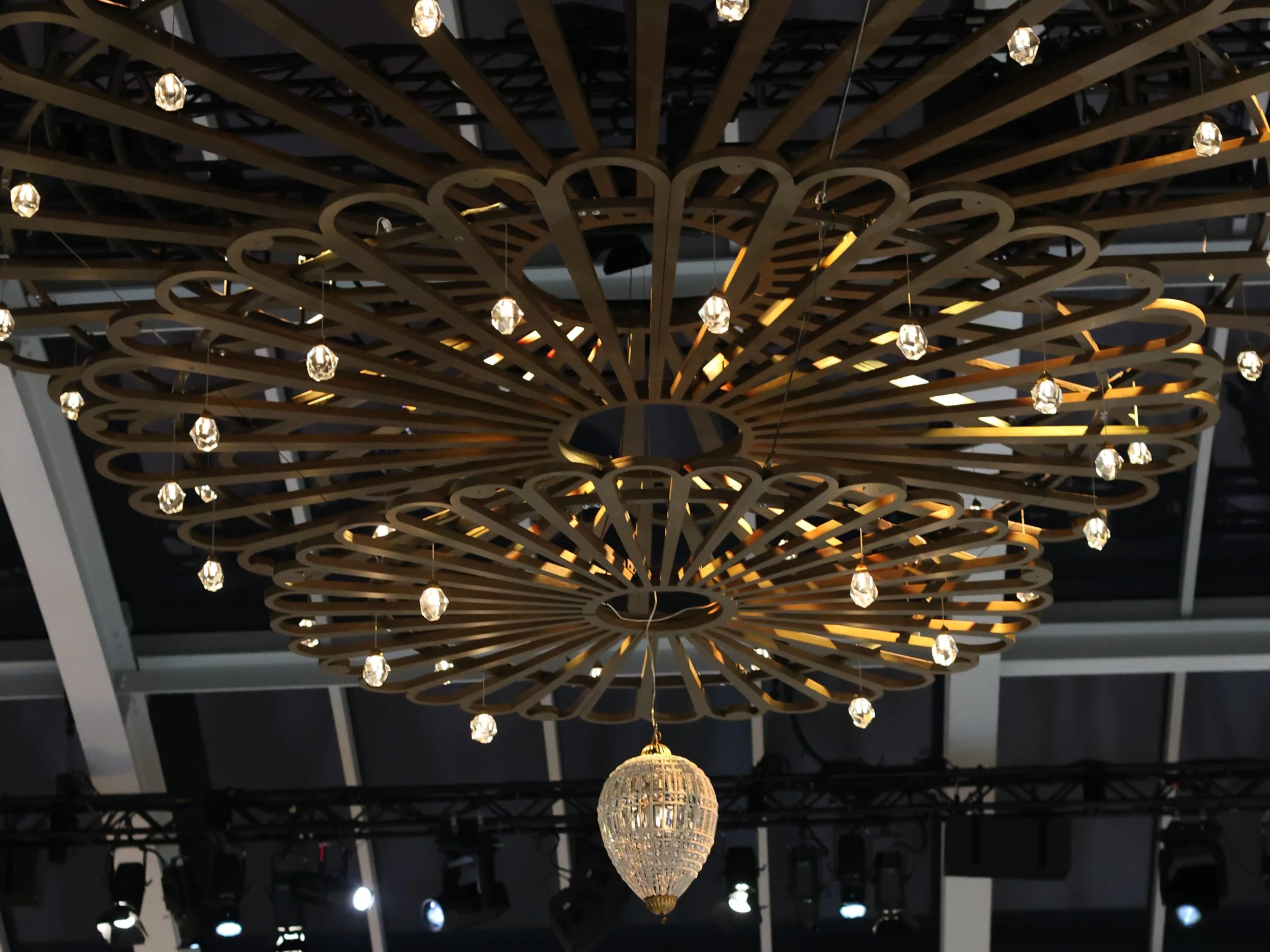 Large wooden chandelier with circular, open design and hanging crystal accents, suspended from ceiling in an indoor space.