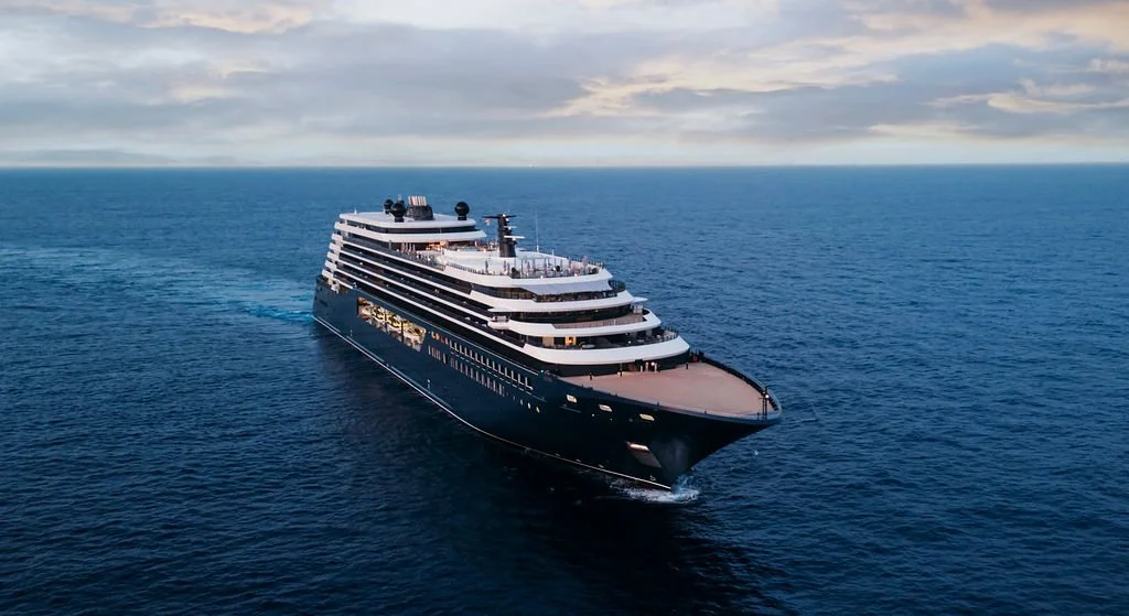 A large luxury cruise ship sailing on the ocean with a cloudy sky in the background.