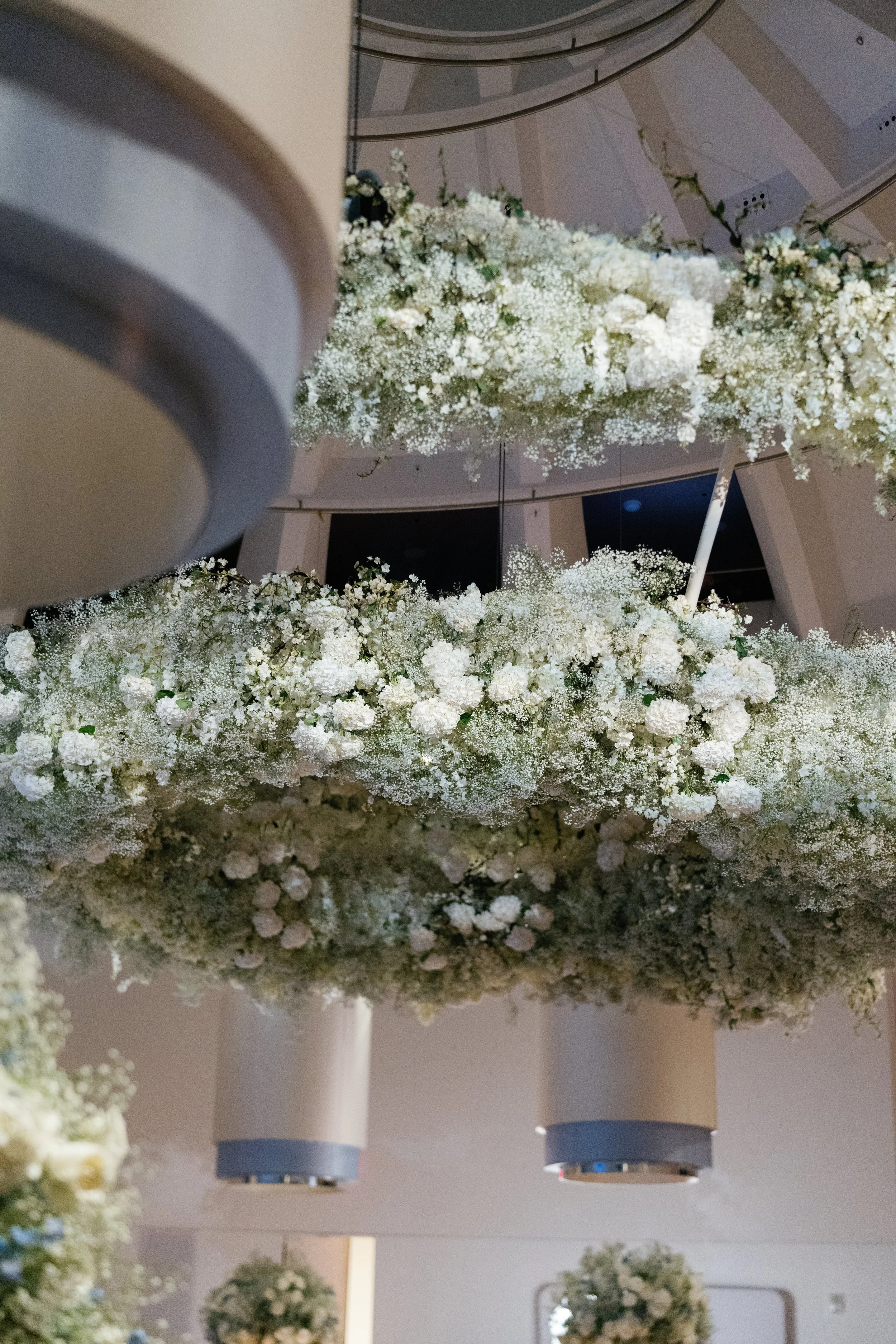 Close-up of a large floral arrangement suspended from the ceiling, featuring white flowers and greenery, in an elegant indoor setting.