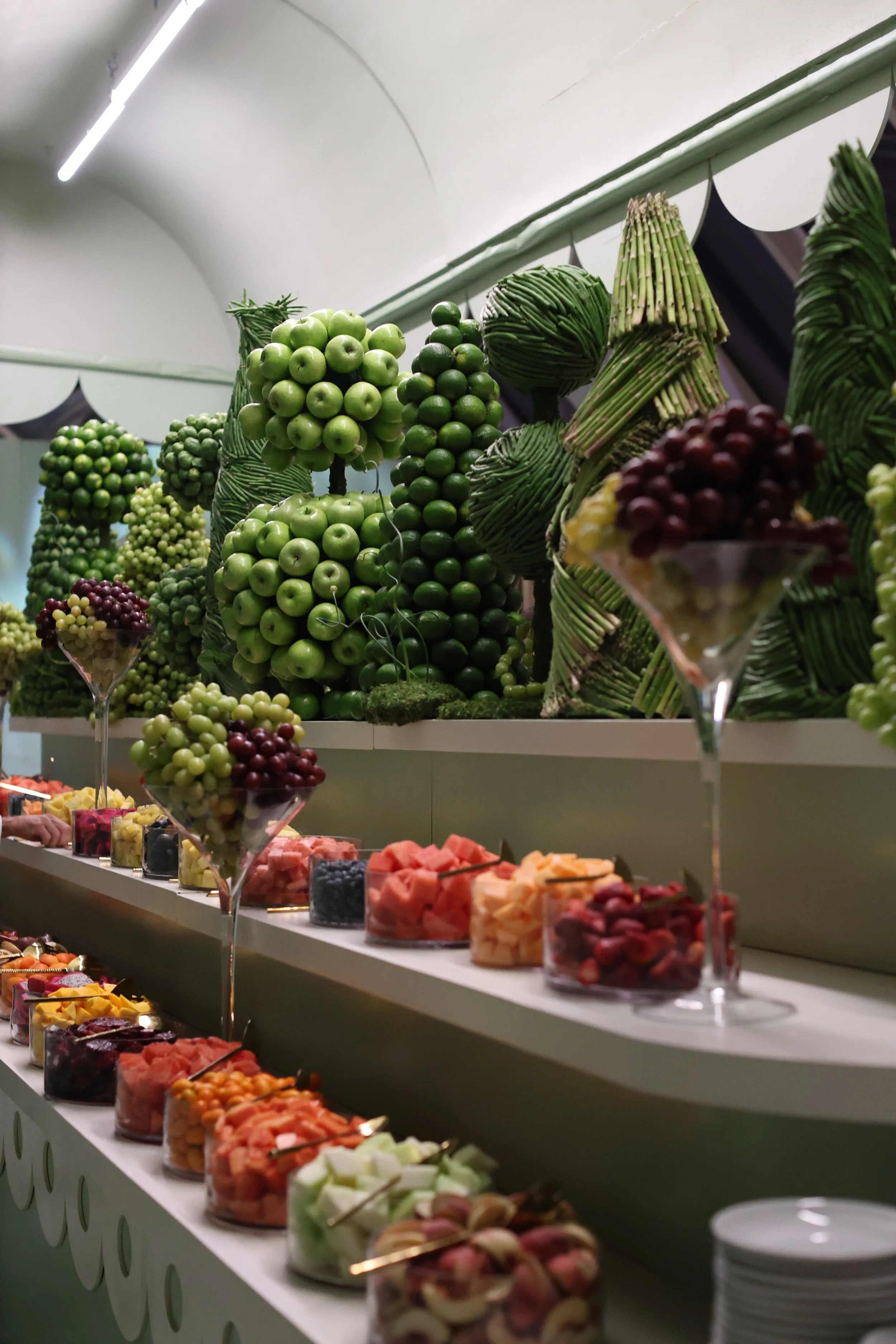 Display of green and purple grapes, arranged with other snacks on a creamy-colored table in a well-lit room.