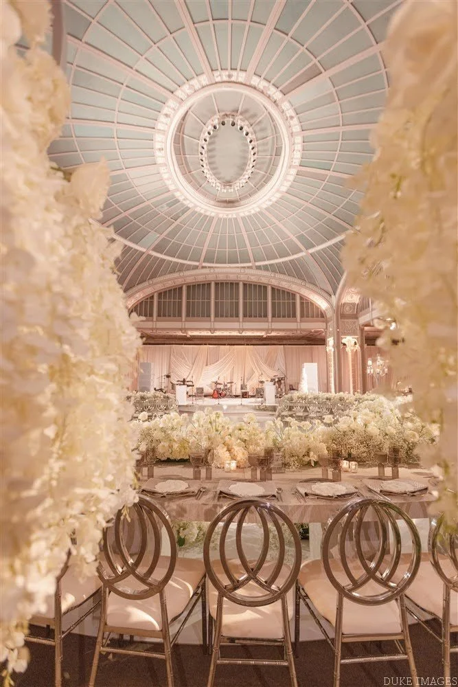 Elegant event space with a grand stage, floral arrangements, and a domed ceiling with a chandelier