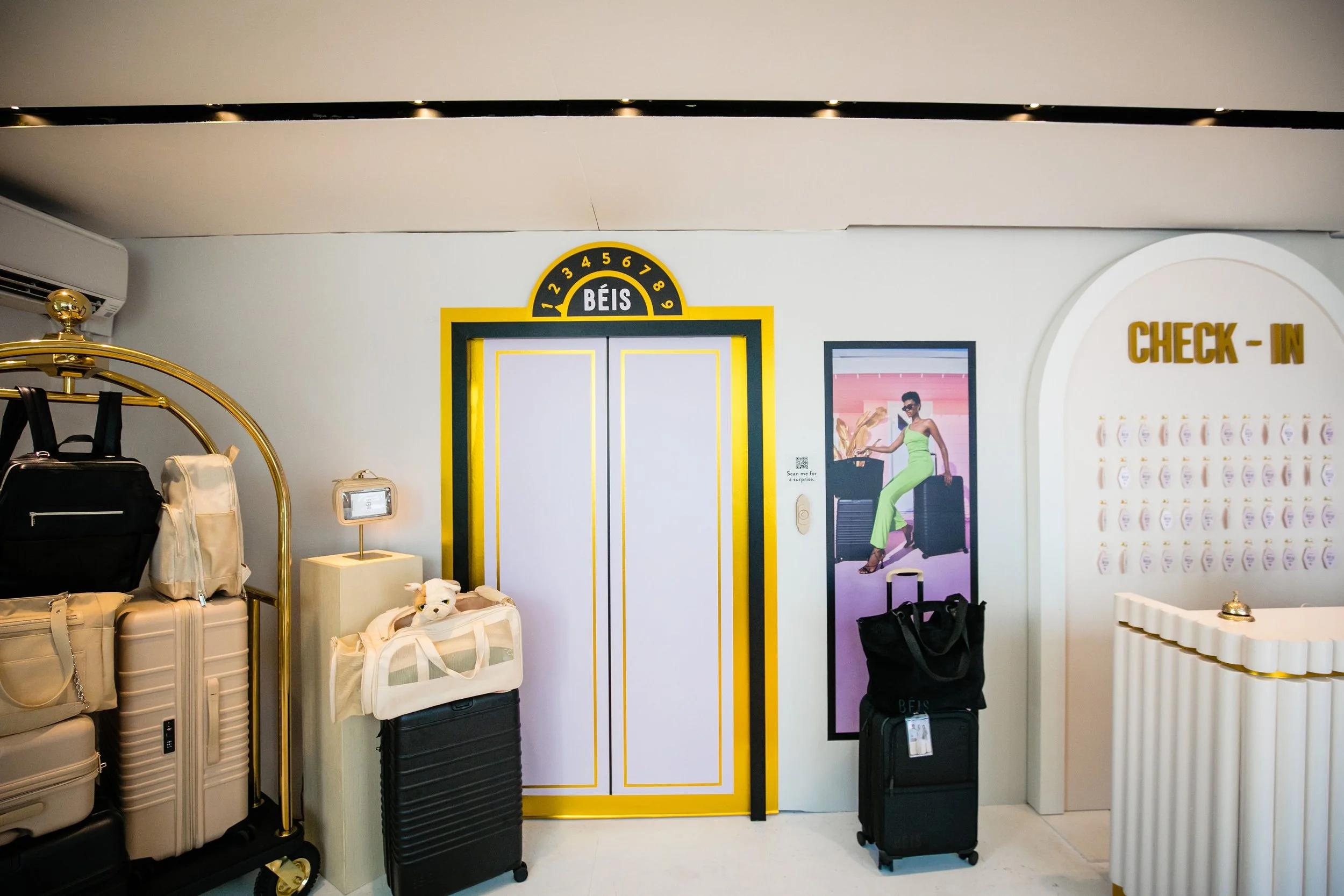 Hotel check-in area with luggage, elevator door, and signage for check-in from an airport lounge decorated in white, gold, and black accents.