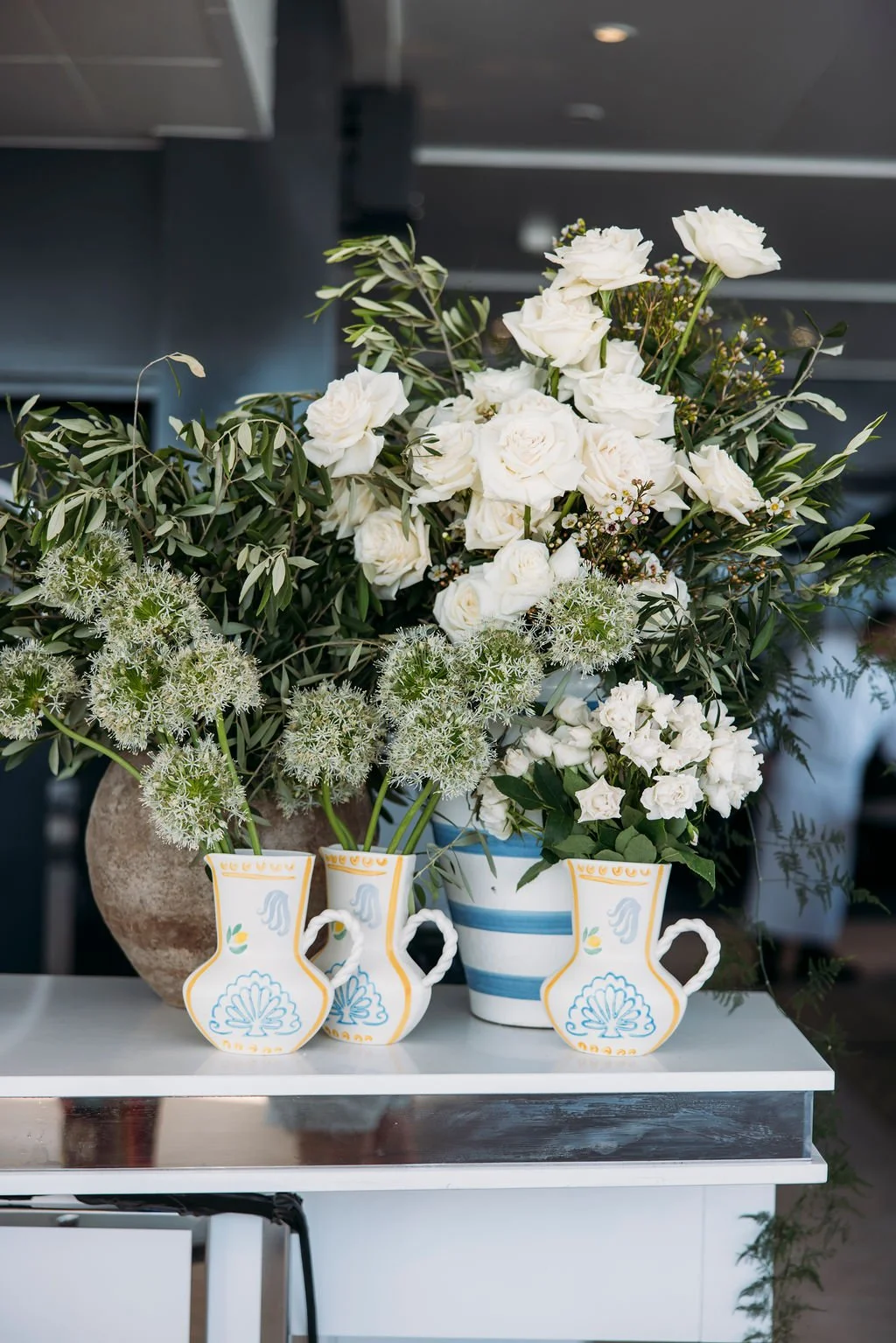 Flower arrangement of white roses and greenery in decorative vases on a white table.