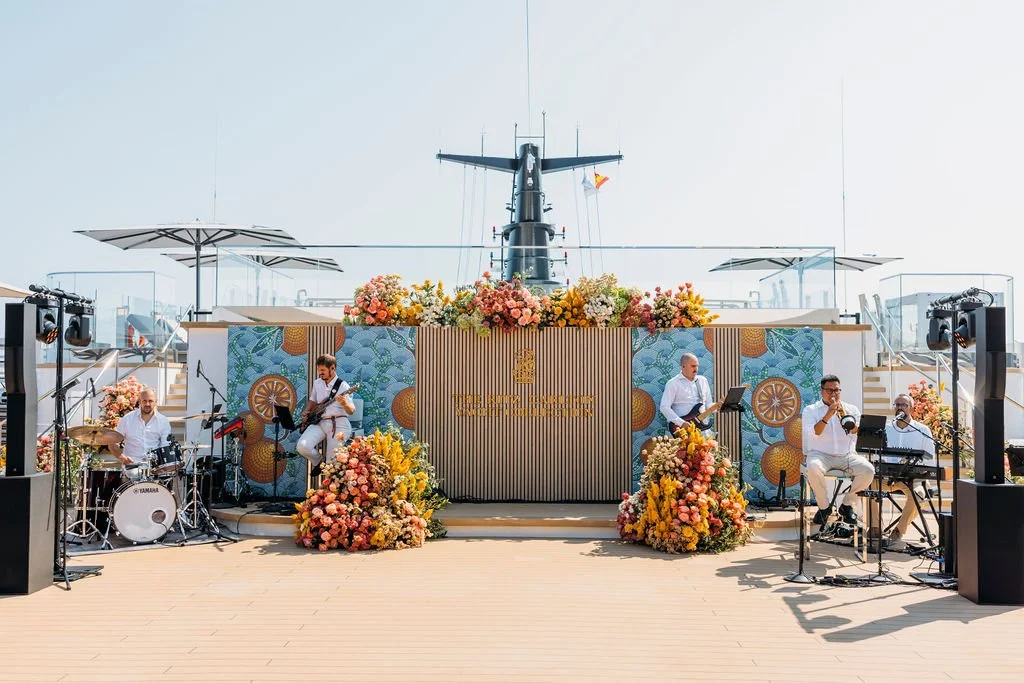A live band performing on a deck with a helicopter in the background decorated with flowers.