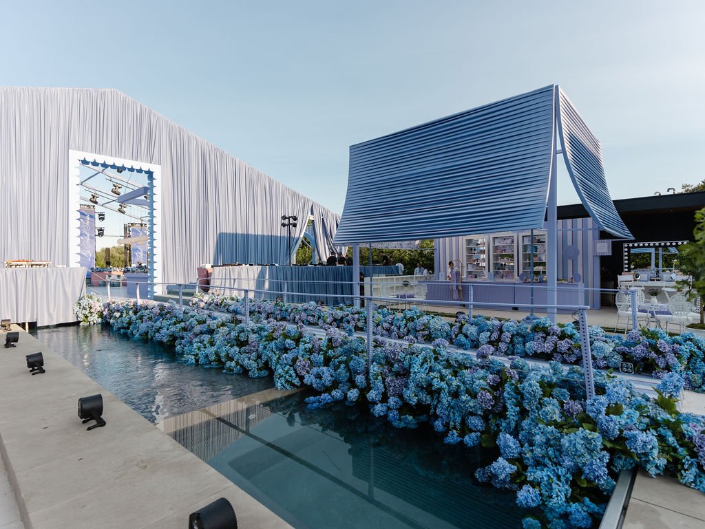 Elegant outdoor event space decorated with blue and white hydrangea flowers, featuring modern architectural structures and a water feature with lighting.