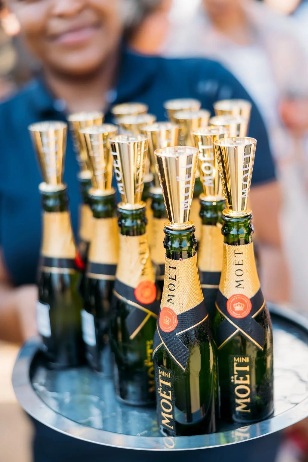 Multiple bottles of Moët champagne with gold foil tops, arranged on a silver tray at a celebration event.