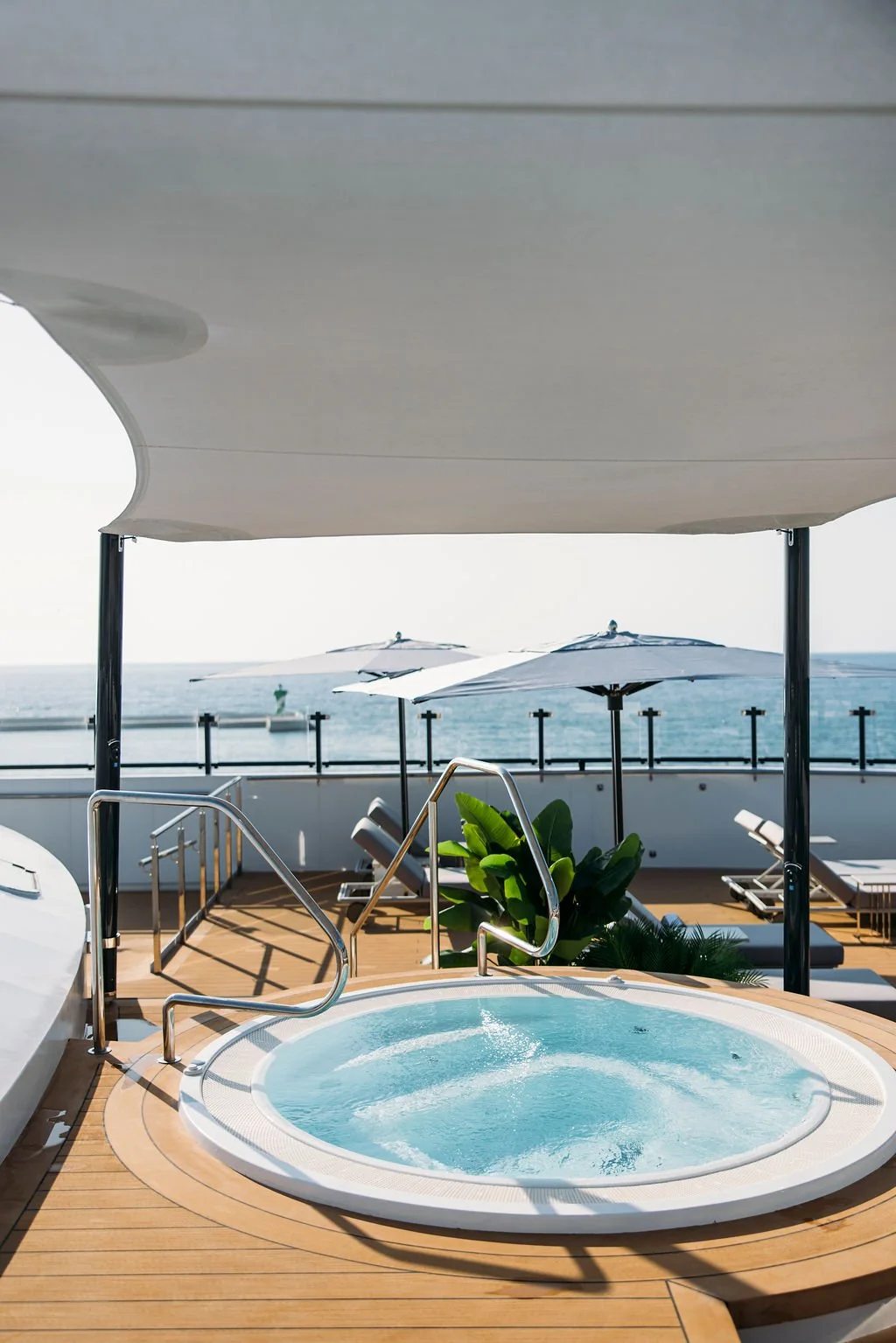 Hot tub on a deck with an ocean view, umbrellas, and lounge chairs in the background.